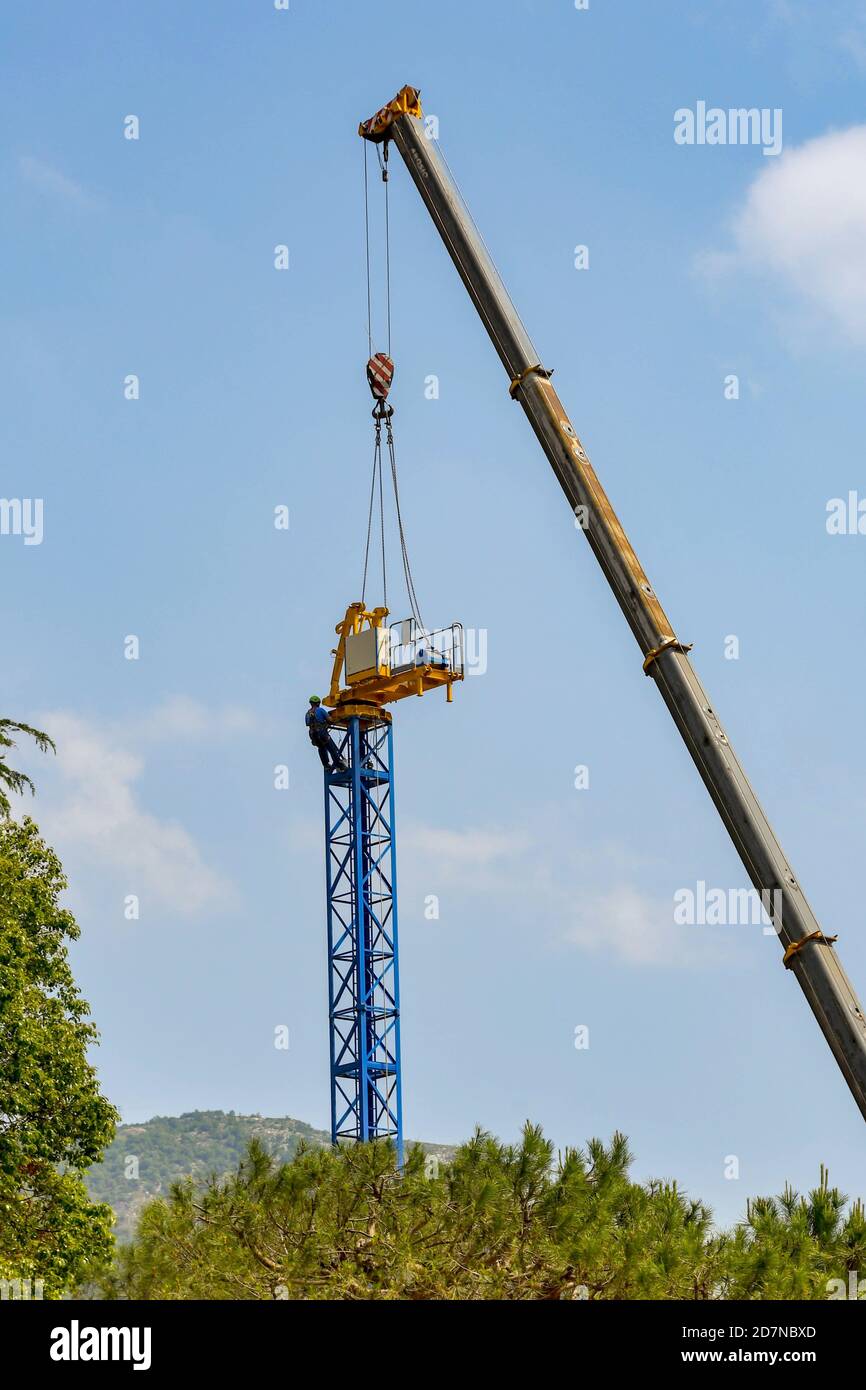 LENNO, COMER SEE, ITALIEN - JUNI 2019: Facharbeiter mit Gurtzeug auf einem Turmkran, der mit Hilfe eines Teleskopkran demontiert wird Stockfoto