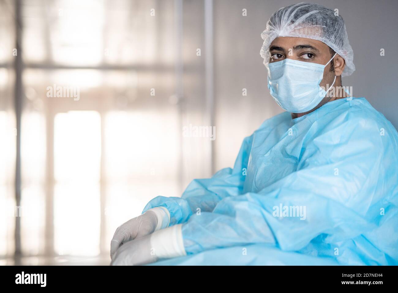 Erschöpfter männlicher Chirurg in schützender Arbeitskleidung, die sich gegen die Wand lehnt Korridor Stockfoto