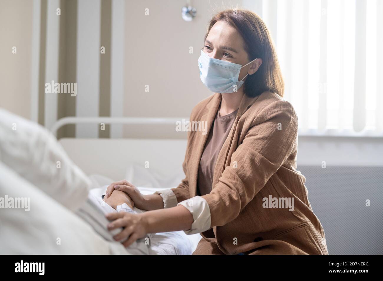 Junge Frau in Casualwear und Schutzmaske berühren Hände Kranker Freund Stockfoto