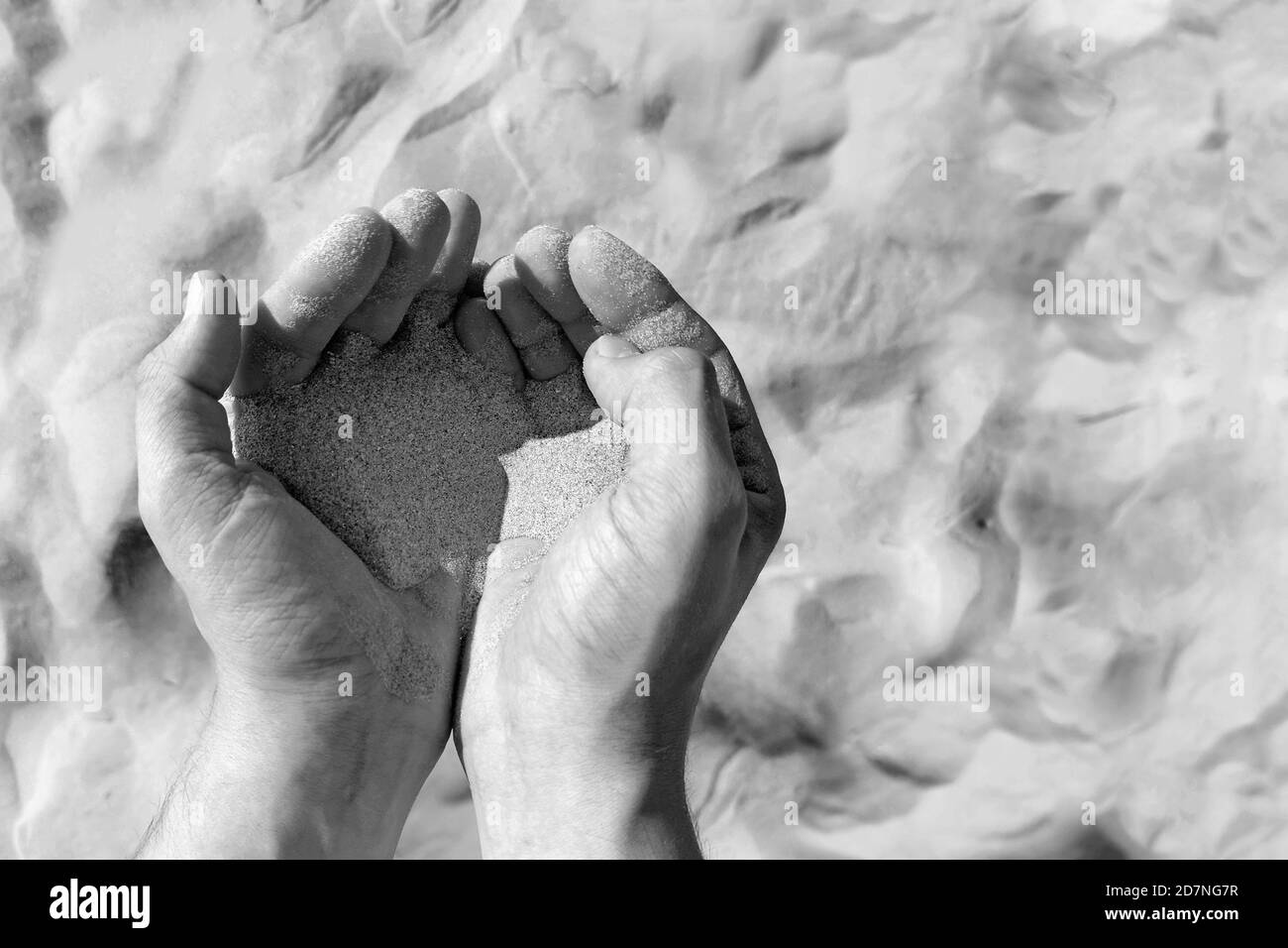 Sand in männlichen Händen auf Sand / Wüste Hintergrund. Schwarzweiß-Foto Stockfoto