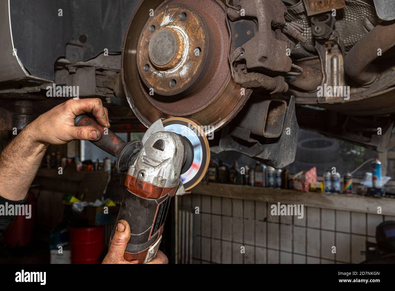 Ein Mechaniker grinst, mit einem Winkelschleifer, die Kante einer alten hinteren Bremsscheibe in einem Auto, Regeneration des Bremssystems. Stockfoto