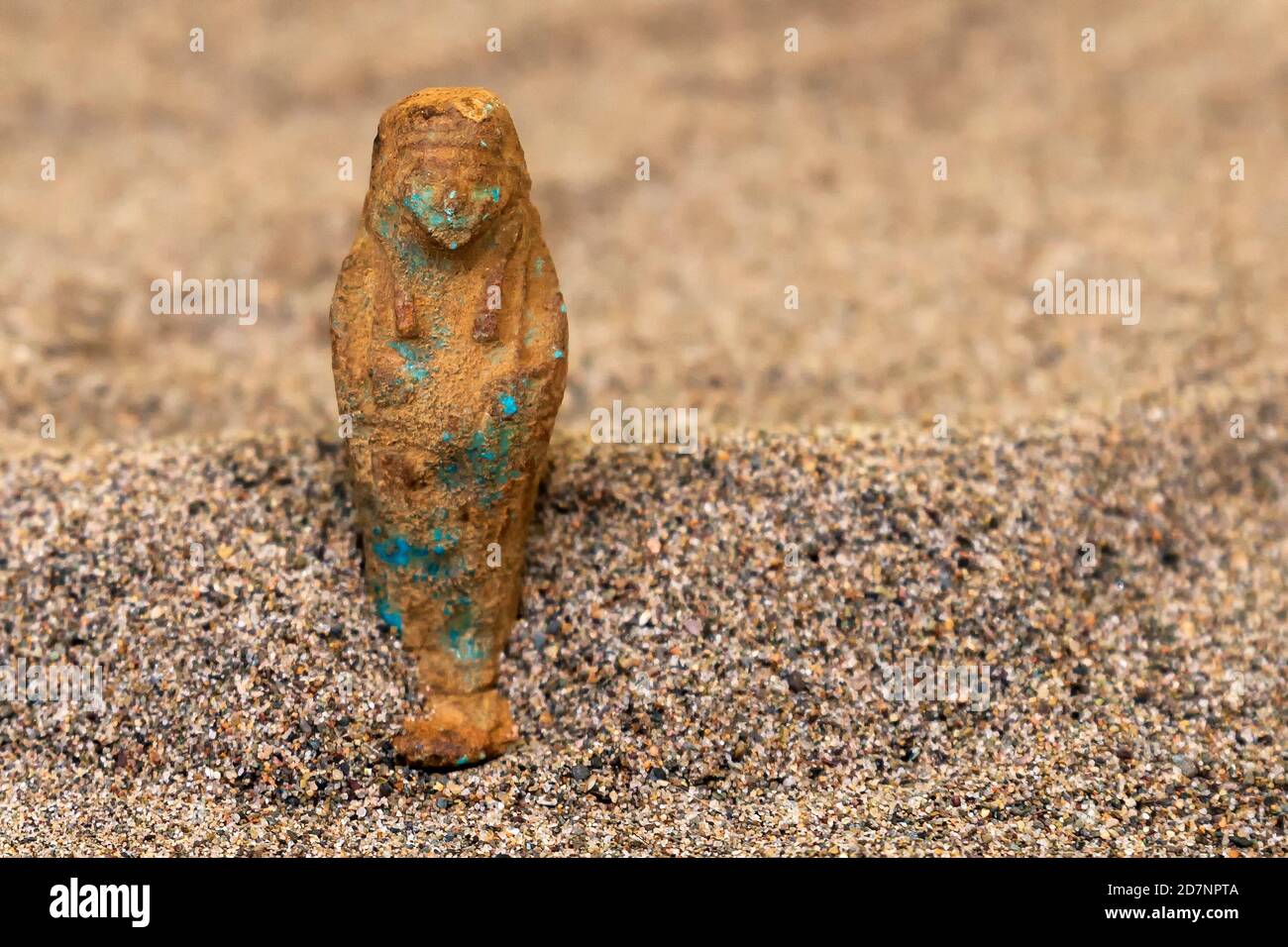 Ein alter, sehr abgenutzter ägyptischer Shabti, der im Sand steht. Geringe Schärfentiefe. Stockfoto