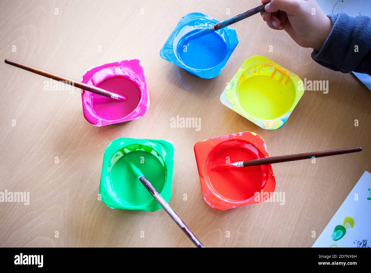 Kind Hand einweichen Künstler Pinsel auf waschbare Tempera Farbe. Joghurtbecher als Farbbehälter wiederverwendet Stockfoto