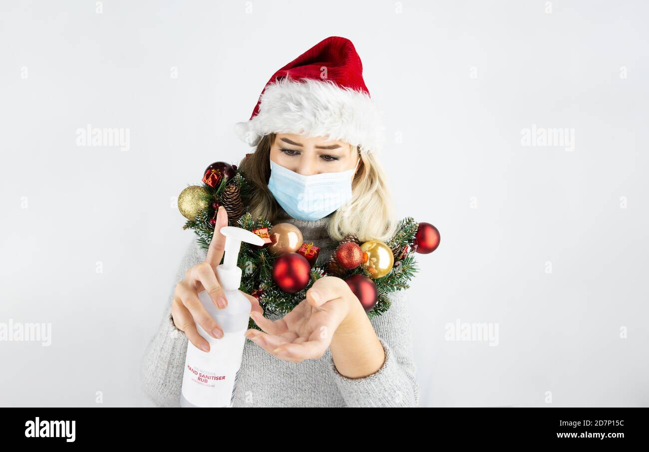 Frauen tragen Weihnachtsmann Hut, eine Maske und Weihnachtskranz und halten Hand Desinfektionsmittel. Stockfoto
