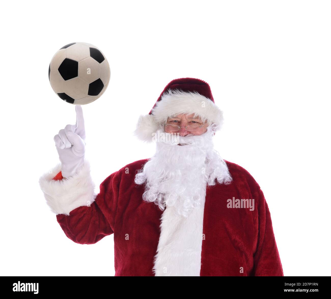 Der Weihnachtsmann zeigt mit seinem Zeigefinger nach oben, mit einem Fußball, der auf der Spitze balanciert ist, isoliert auf Weiß. Stockfoto