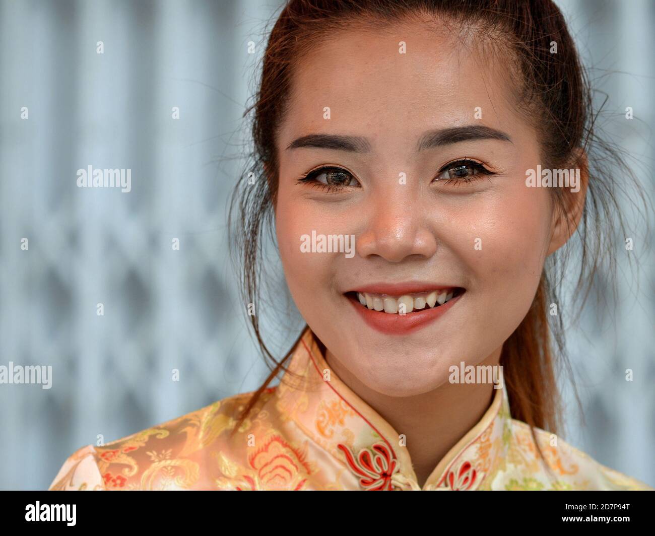 Schöne junge Thai chinesische Frau trägt ein traditionelles chinesisches Kleid (Cheongsam) und lächelt für die Kamera während des chinesischen Neujahrs. Stockfoto