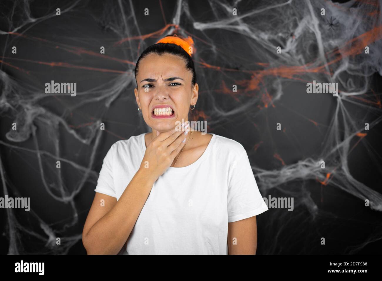 Junge schöne Frau auf schwarzem Hintergrund mit Spinnweben und Spinnen berühren schmerzhaften Hals, Halsschmerzen für Grippe, Klumpen und Infektion Stockfoto