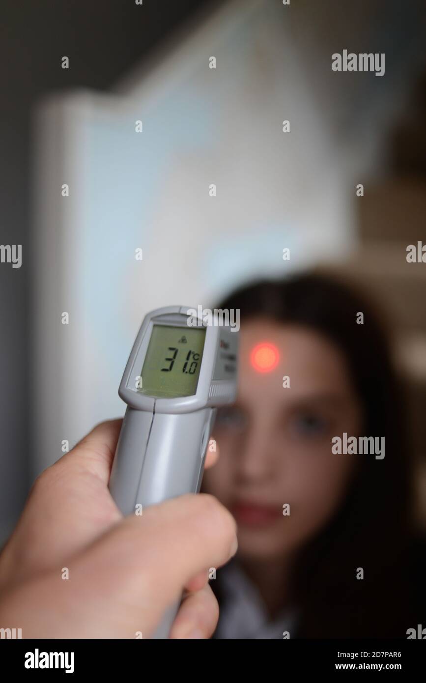 Verwenden eines Infrarot-Thermometers, um die Körpertemperatur eines Kindes zu überprüfen, bevor es während der Covid19-Pandemie zur Schule geht. Stockfoto