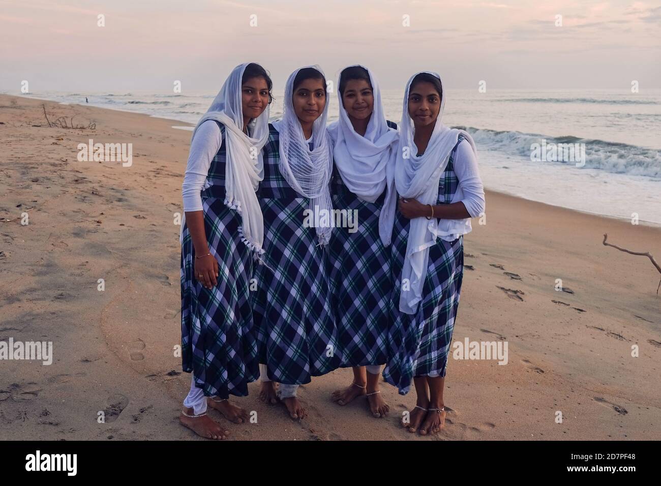 Vier junge indische Mädchen, Schwestern aus lokalen armen hindu-Familie, tragen ähnliche Kleider und weiße drapierten Kopftücher laufen barfuß am Meeresstrand Stockfoto