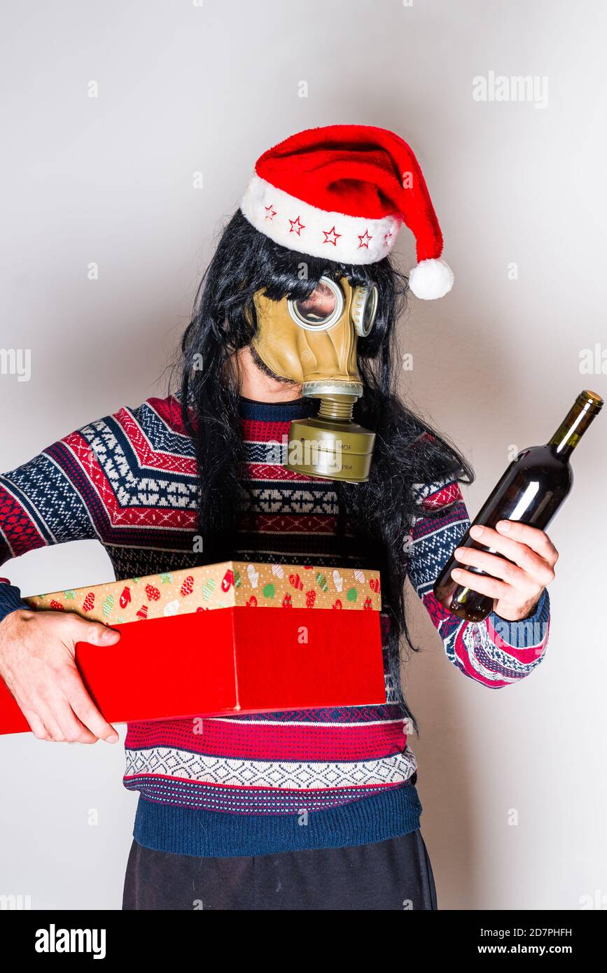 Person mit langen schwarzen Haaren in Gasmaske und weihnachten hut mit Geschenk und Flasche Wein in Händen Heller Hintergrund Stockfoto