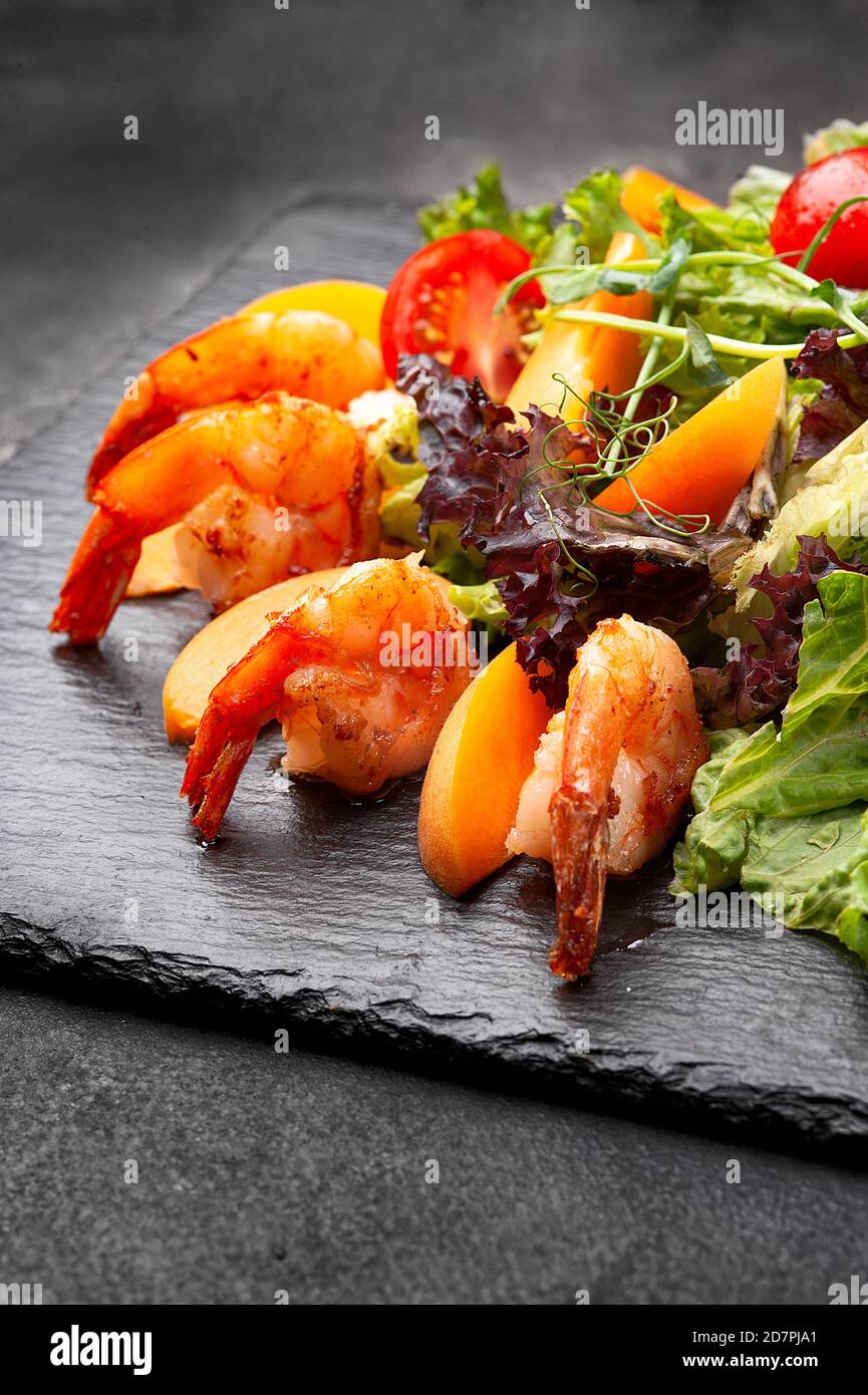 Frischer Salat mit Garnelen auf schwarzem Teller. Stockfoto