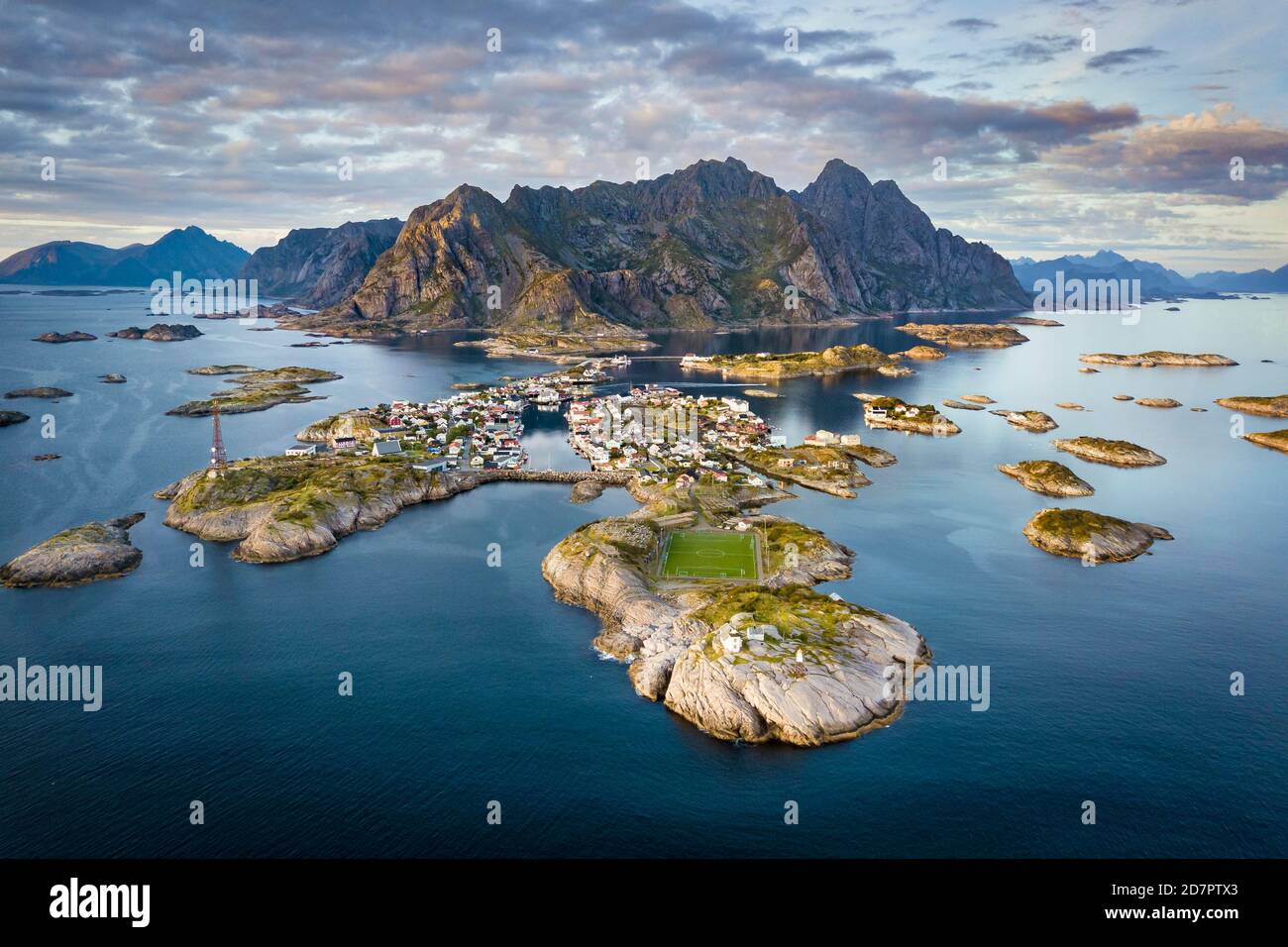 Luftaufnahme der Inselwelt in der Nähe des Fischerdorfes Henningsvaer, vor Halbinsel mit Fußballplatz, im hinteren Bergmassiv Vagakallen Stockfoto