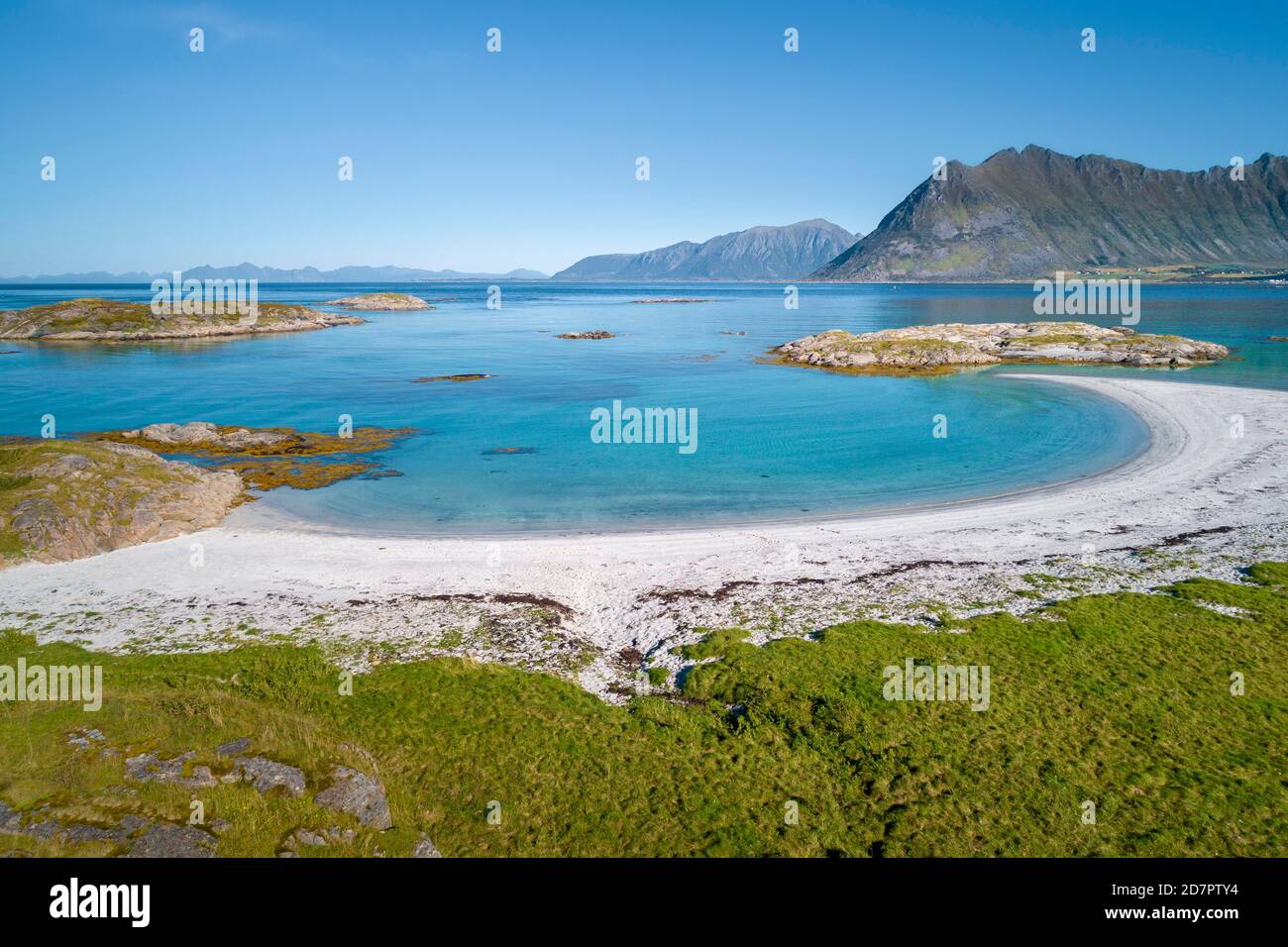 Halbmondförmige Bucht, weißer Sandstrand, türkisfarbenes Meer, grasige Küste vorne, steile Berge dahinter, Vagan, Lofoten, Nordland, Norwegen Stockfoto