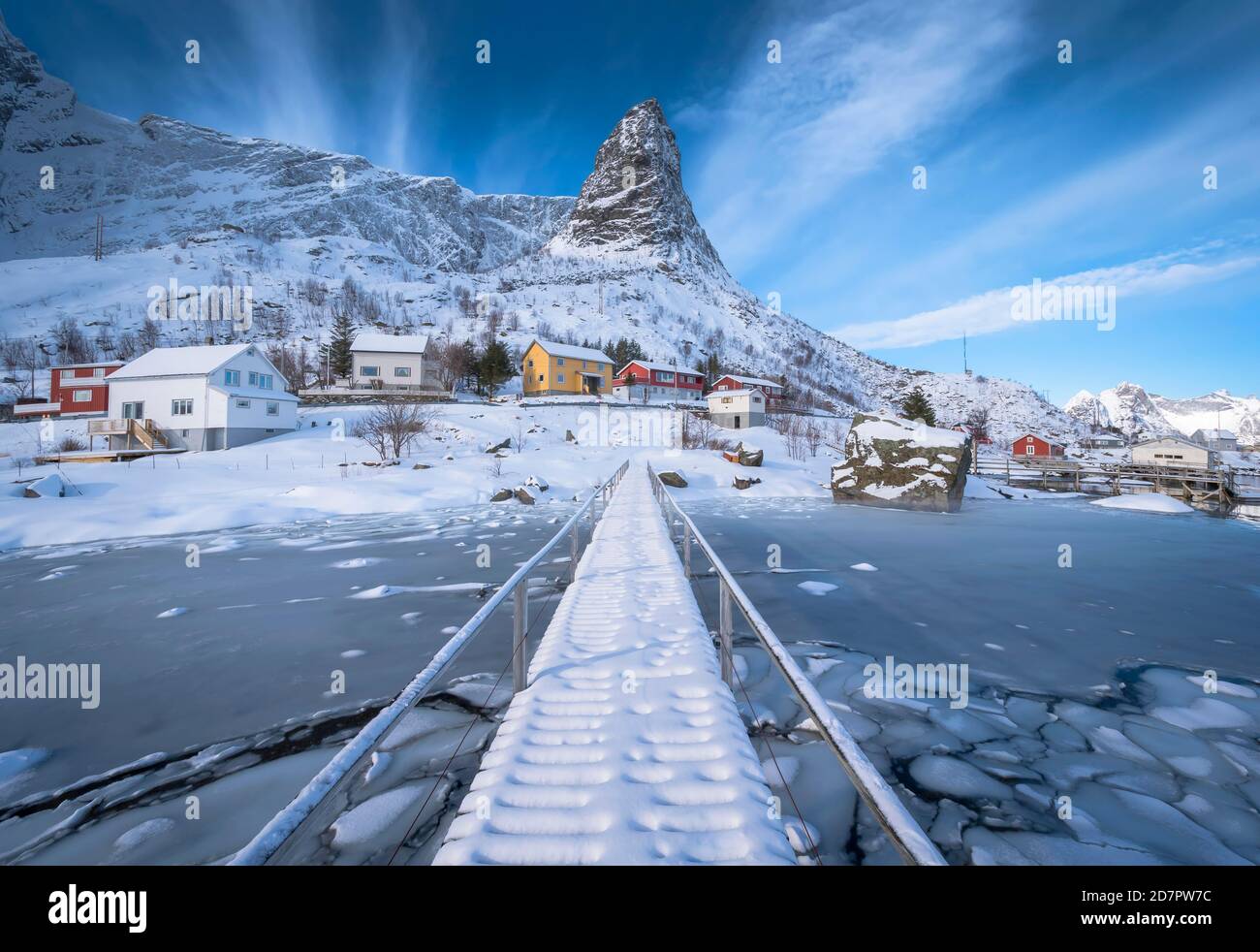 Fußgängerbrücke über gefrorenen Fjord, im Hintergrund Wohnhäuser in verschneite Landschaft und Bergformation Hammarskaftet, Nordland, Lofoten, Norwegen Stockfoto
