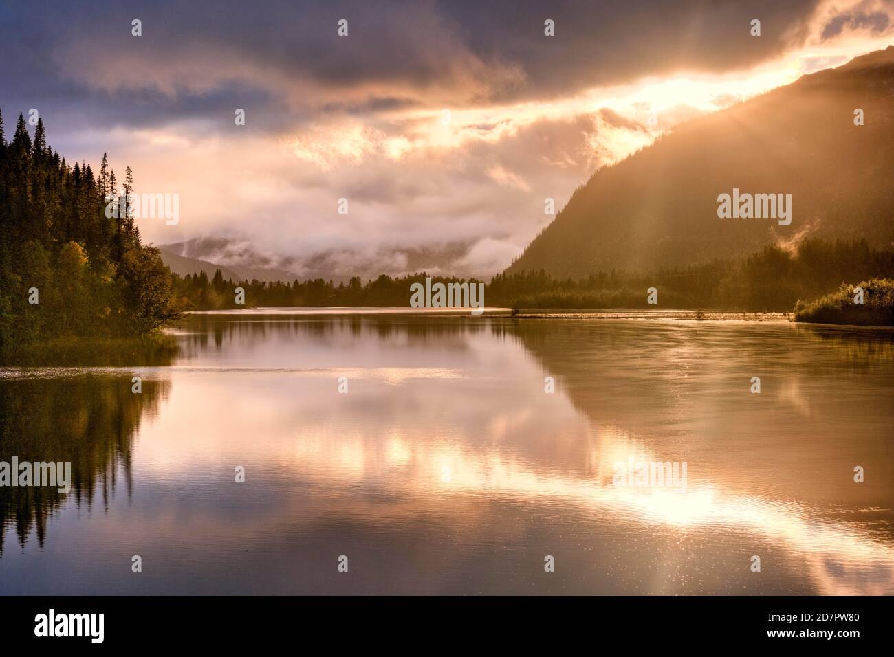 Stimmungsvoller Sonnenuntergang an einem bewaldeten See, Bergen und woklienbank im Hintergrund Stockfoto