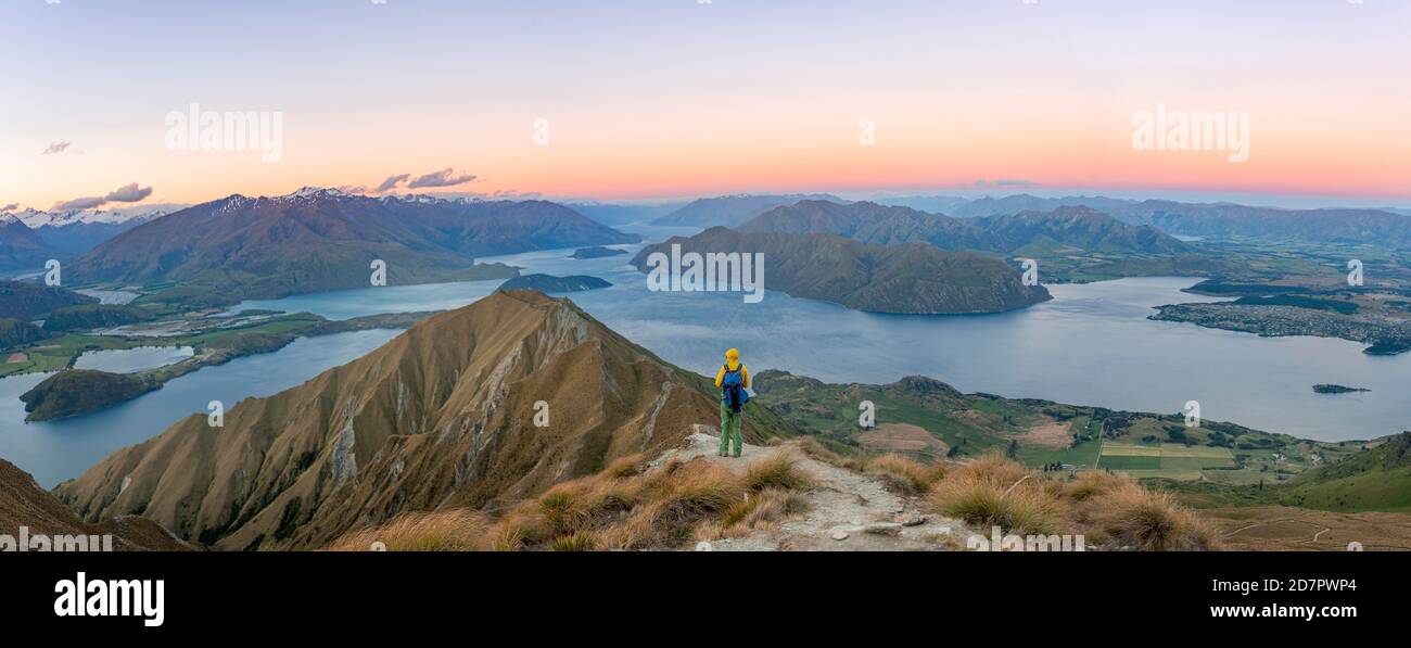 Junger Mann auf dem Gipfel, Blick auf Berge und See vom Mount Roy, Roys Peak bei Sonnenuntergang, Lake Wanaka, Southern Alps, Otago, South Island Stockfoto
