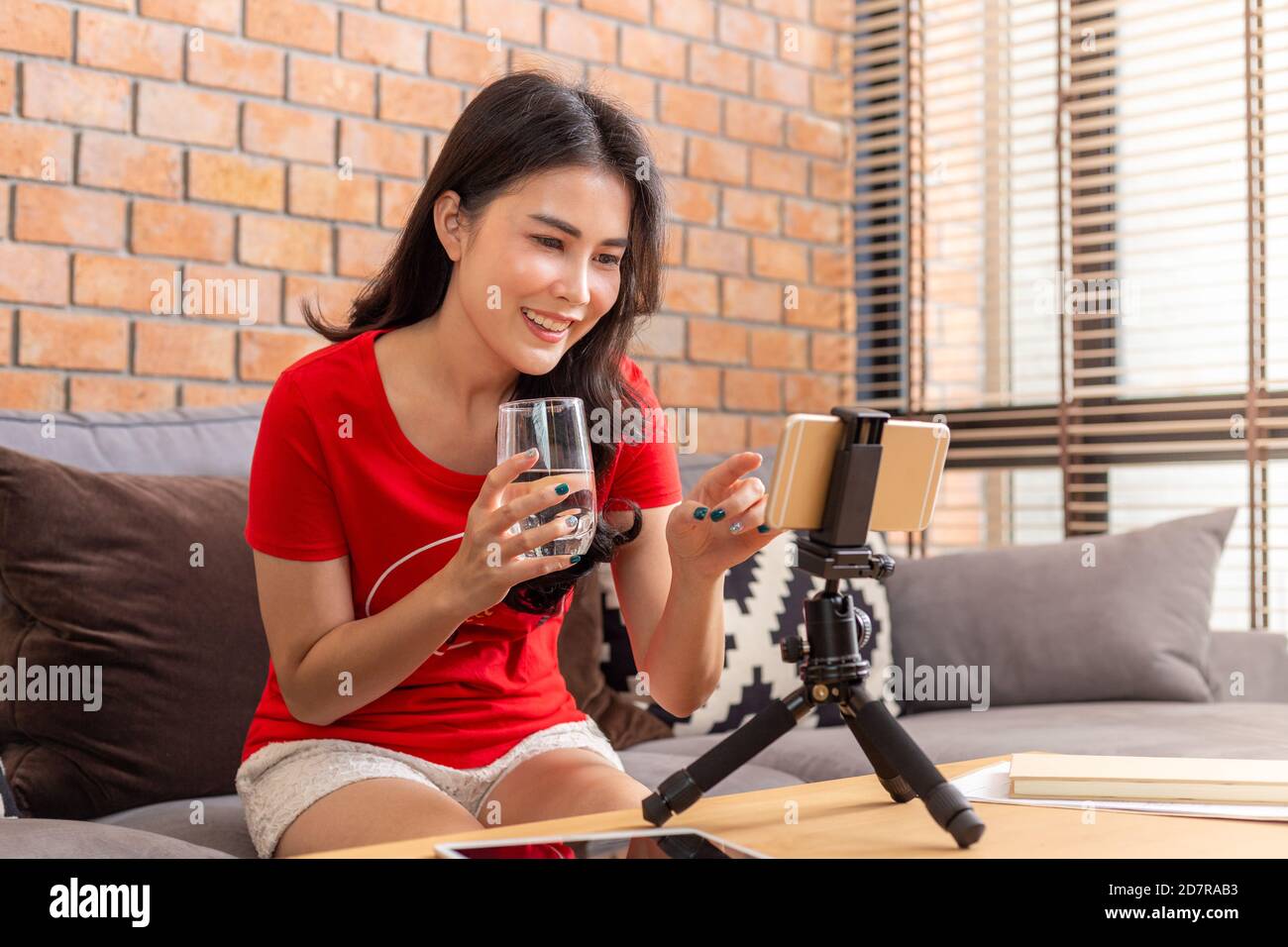 Glücklich junge asiatische Frau in ihrem Casual Kleidung halten trinken Glas Wasser während der Verbindung mit ihren Online-Freunden oder Ihre Fanseite durch ihre sma Stockfoto