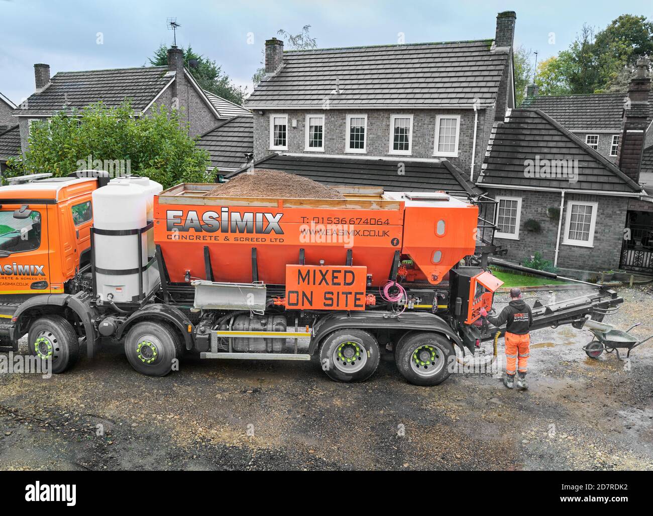 Der Arbeiter mischt Beton vor Ort aus einem Easimix-Lastwagen in eine Schubkarre für eine neue Auffahrt. Stockfoto