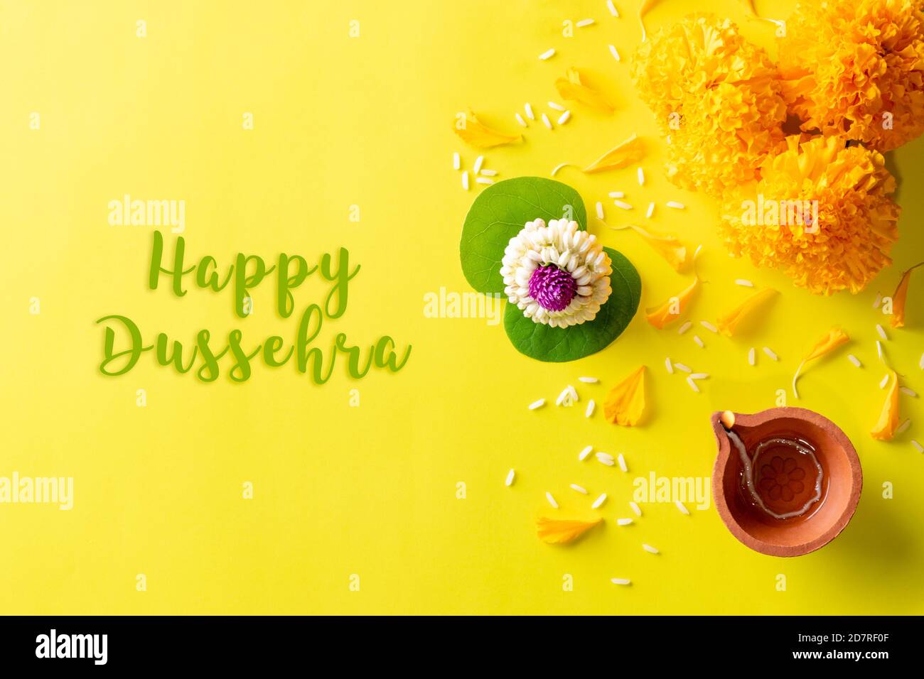 Diya-Lampen aus Ton, die während der Dussehra mit gelben Blüten, grünem Blatt und Reis auf gelbem Hintergrund leuchten. Dussehra Indian Festival Konzept. Stockfoto