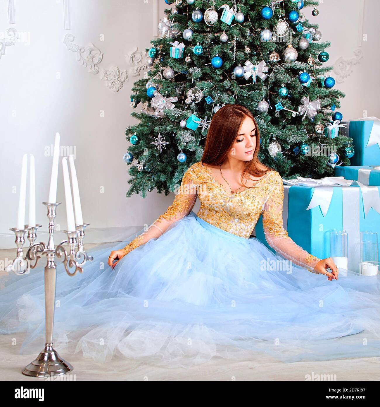 Junge und glückliche Frau in langen Kleid sitzt in der Nähe Weihnachtsbaum mit Weihnachtsspielzeug in festlichen Studio. Winterpostkarte. Weihnachtskarte. Stockfoto