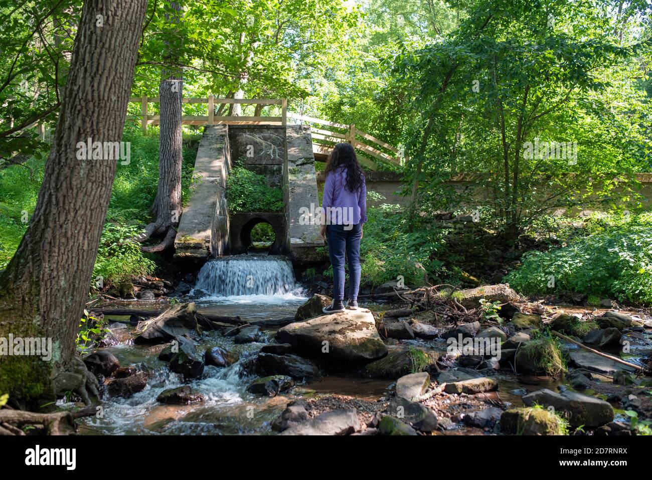 Junger Mann, der alleine am Fuß eines Waldwasserfalls wandert. Stockfoto