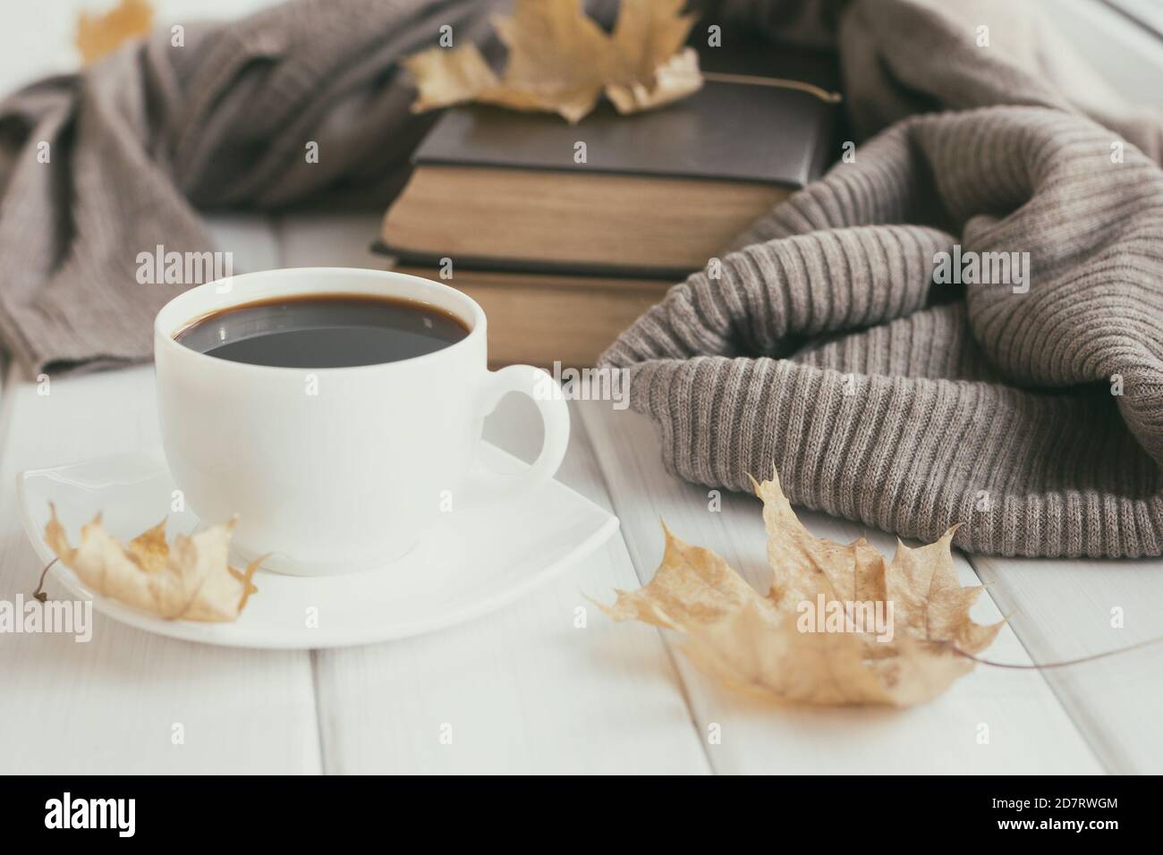 Warmer Wollpullover, Tasse Kaffee, alte Bücher mit Herbstblättern auf weißen Holzbrettern. Gemütliches Haus Lesen, Hygge Konzept Stockfoto