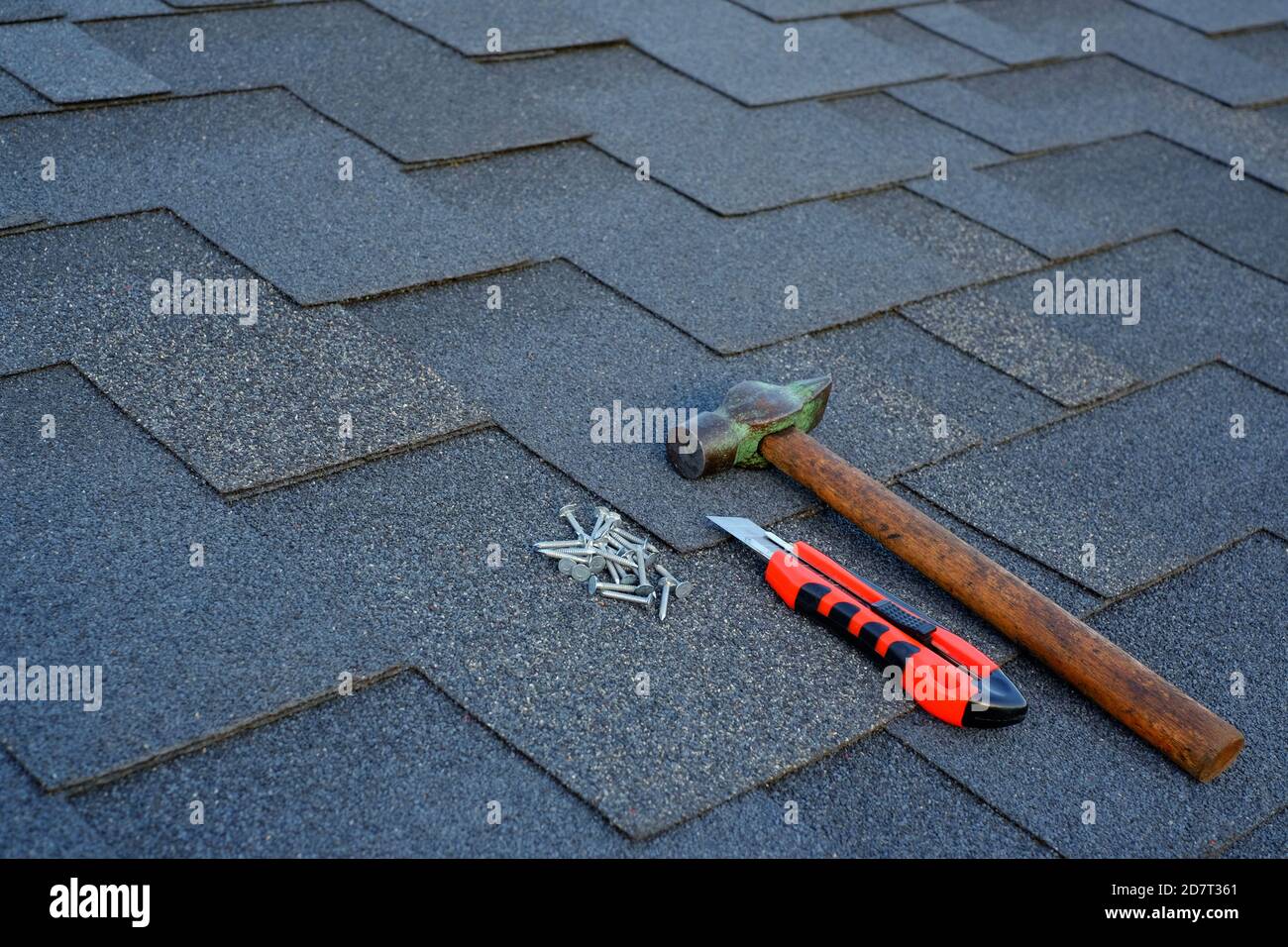 Nahaufnahme Ansicht auf Asphalt Schindeln auf einem Dach mit Hammer, Nägel und Schreibwaren Messer Hintergrund. Stockfoto