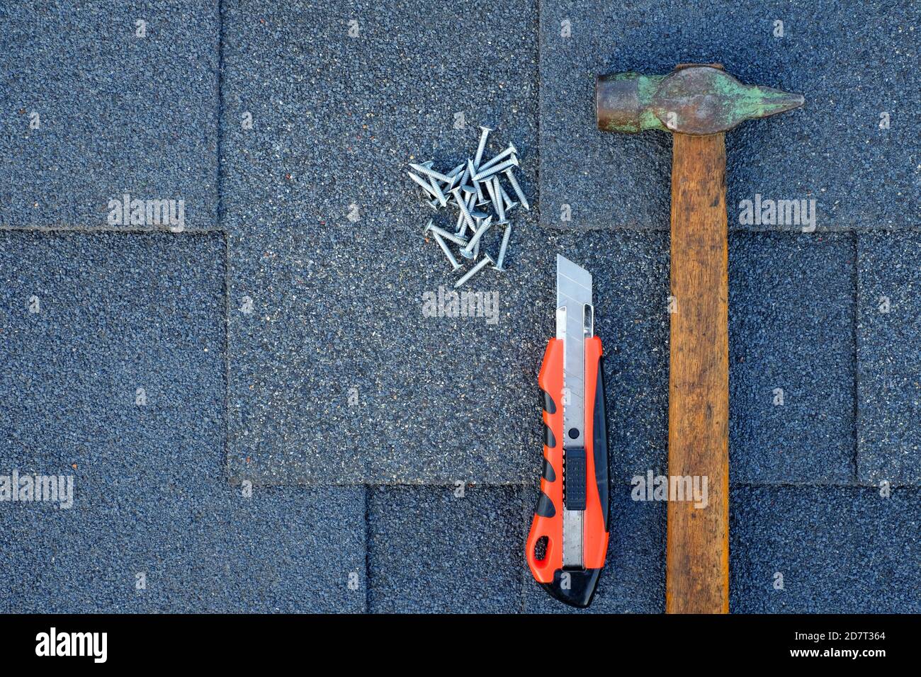 Nahaufnahme auf Asphaltschindeln auf einem Dach mit Hammer, Nägeln und Schreibwarenmesser. Stockfoto
