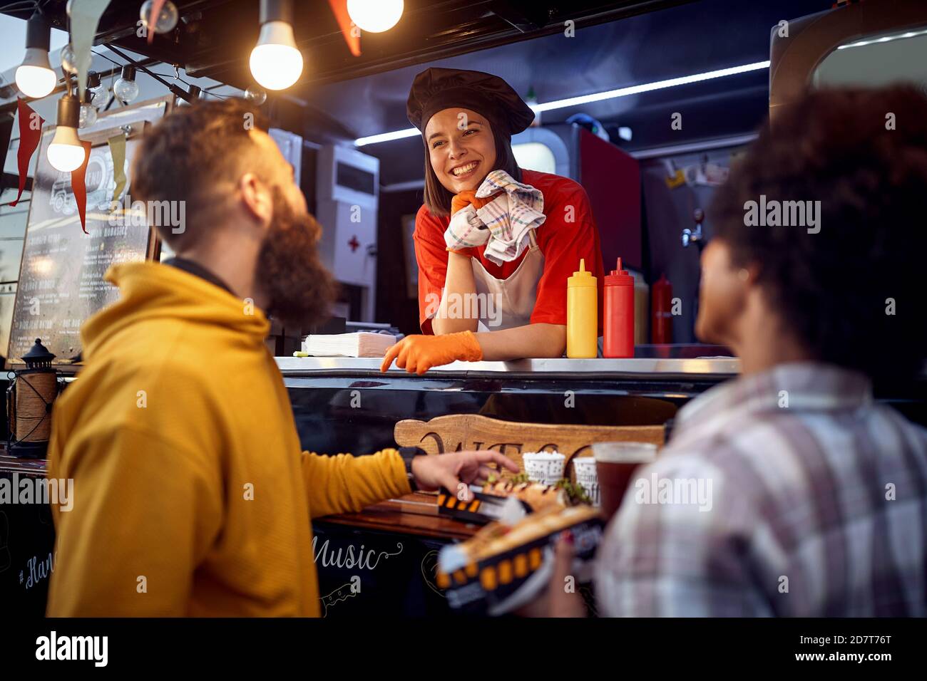 Junge Hipster ist im Begriff, Sandwich vor Fast-Food-Service essen, Blick auf zufriedene Mitarbeiter lächelnd Stockfoto