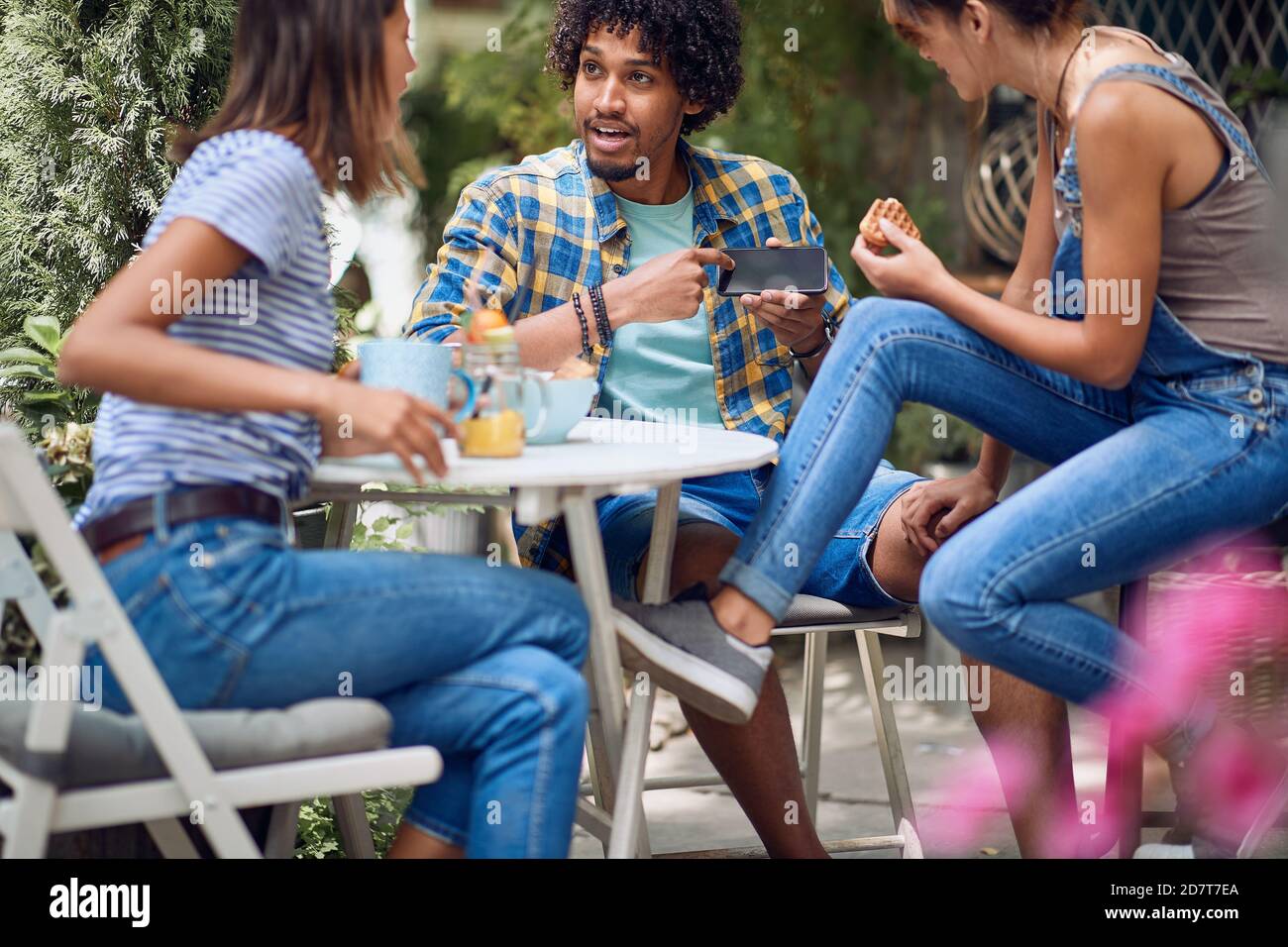 Ein Kerl zeigt Smartphone-Inhalte an seine weiblichen Freunde in der Bar Hinterhof bei einem schönen Wetter. Qualität Freundschaft Zeit zusammen Stockfoto