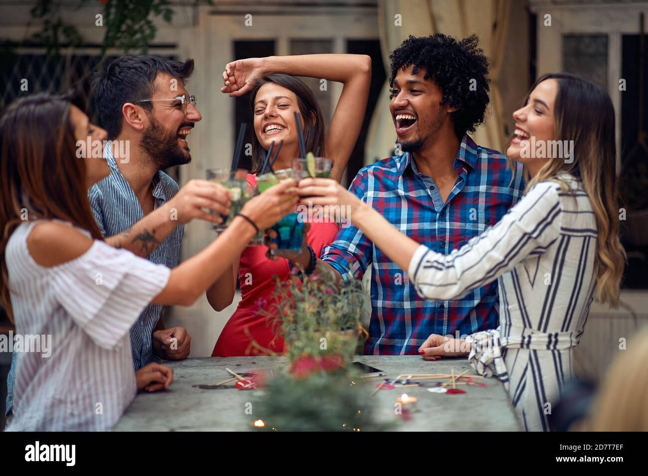 Fröhliche Paare, die auf der Open-Air-Geburtstagsparty in einer schönen Sommerdämmerung anstoßen. Qualität Freundschaft Zeit zusammen Stockfoto