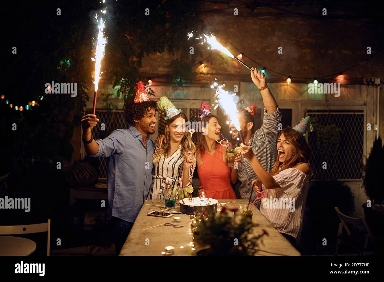 Gruppe von fröhlichen Freunden spielen mit Feuerwerk auf der Open-Air-Geburtstagsparty an einem schönen Sommerabend. Qualität Freundschaft Zeit zusammen Stockfoto