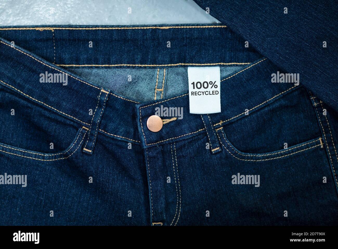 Jeans in recyceltem Blau mit einem Kleidungsanhänger im Inneren. Kreislaufwirtschaftsprinzip, Zero Waste Konzept. Wiederverwendung von Materialien und Reduzierung von Abfall in der Mode. Denim Stockfoto