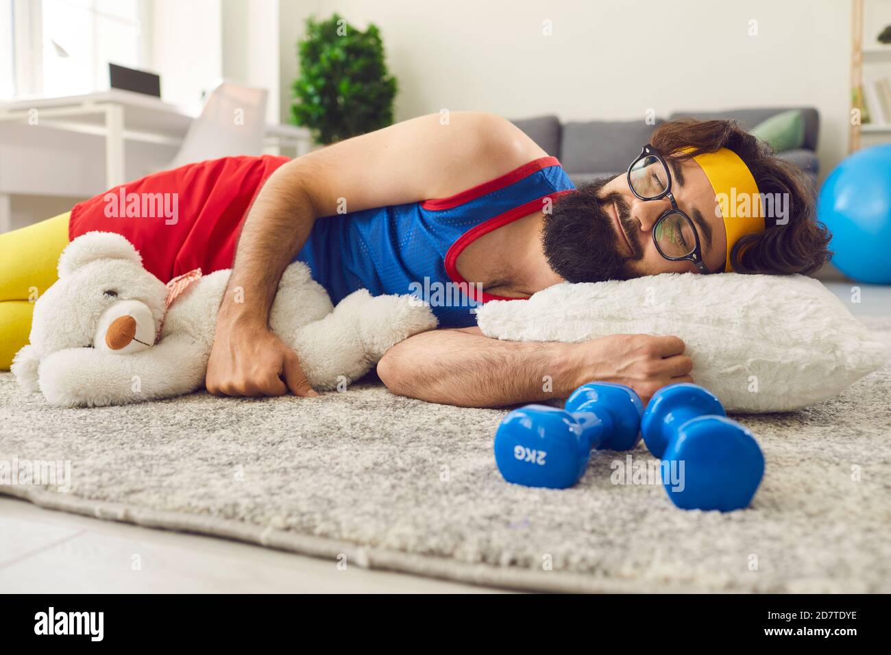 Lustige lächelnde Mann in hellen bunten Sportbekleidung schlafen auf Teppich Mit Spielzeug während des sportlichen Trainings Stockfoto