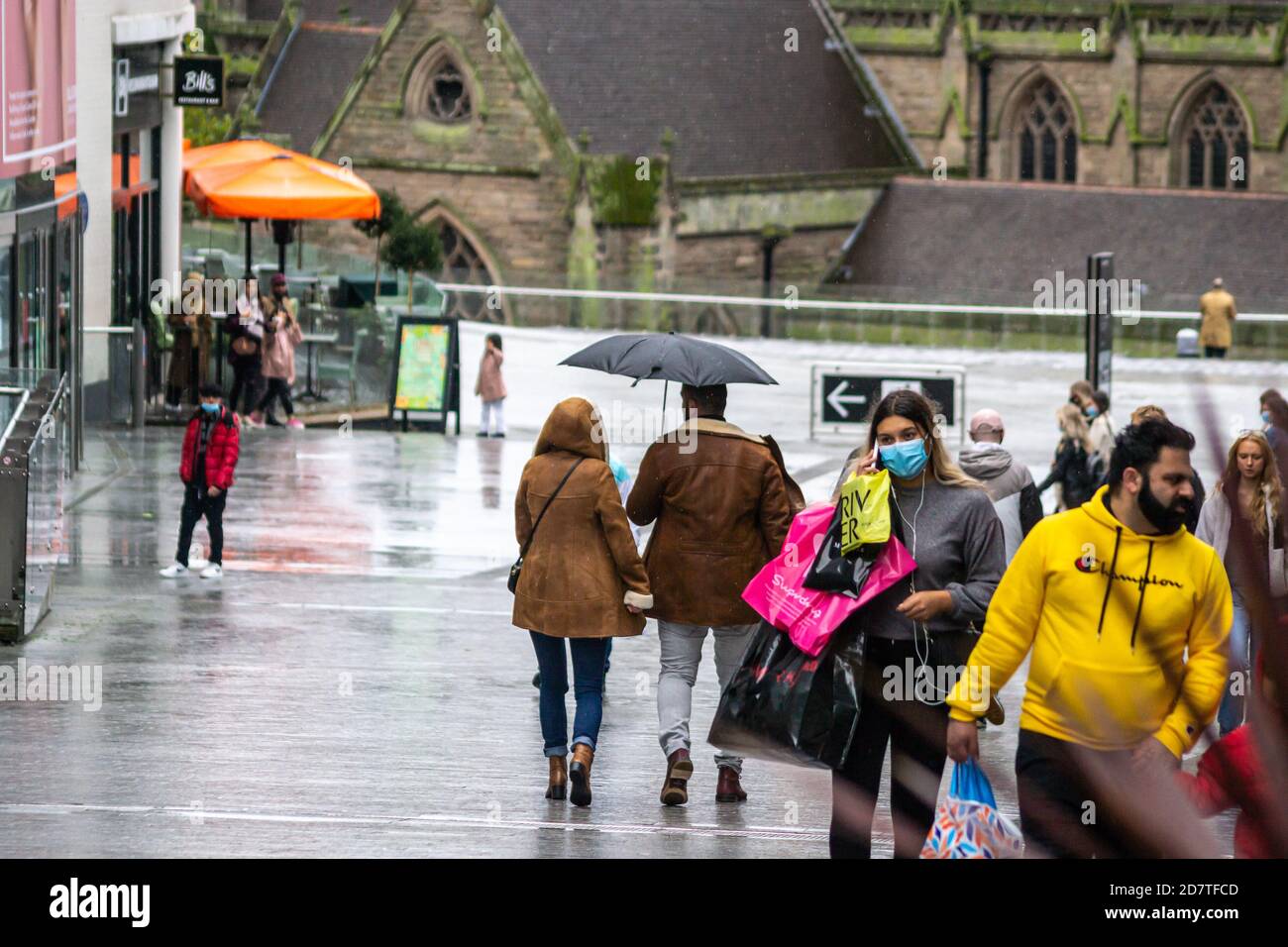 Ein Paar, das bei Regenwetter mit einem Regenschirm durch Birmingham läuft, andere tragen Gesichtsmasken, da sich die Stadt in Covid-19 Alert Tier 2 befindet Stockfoto