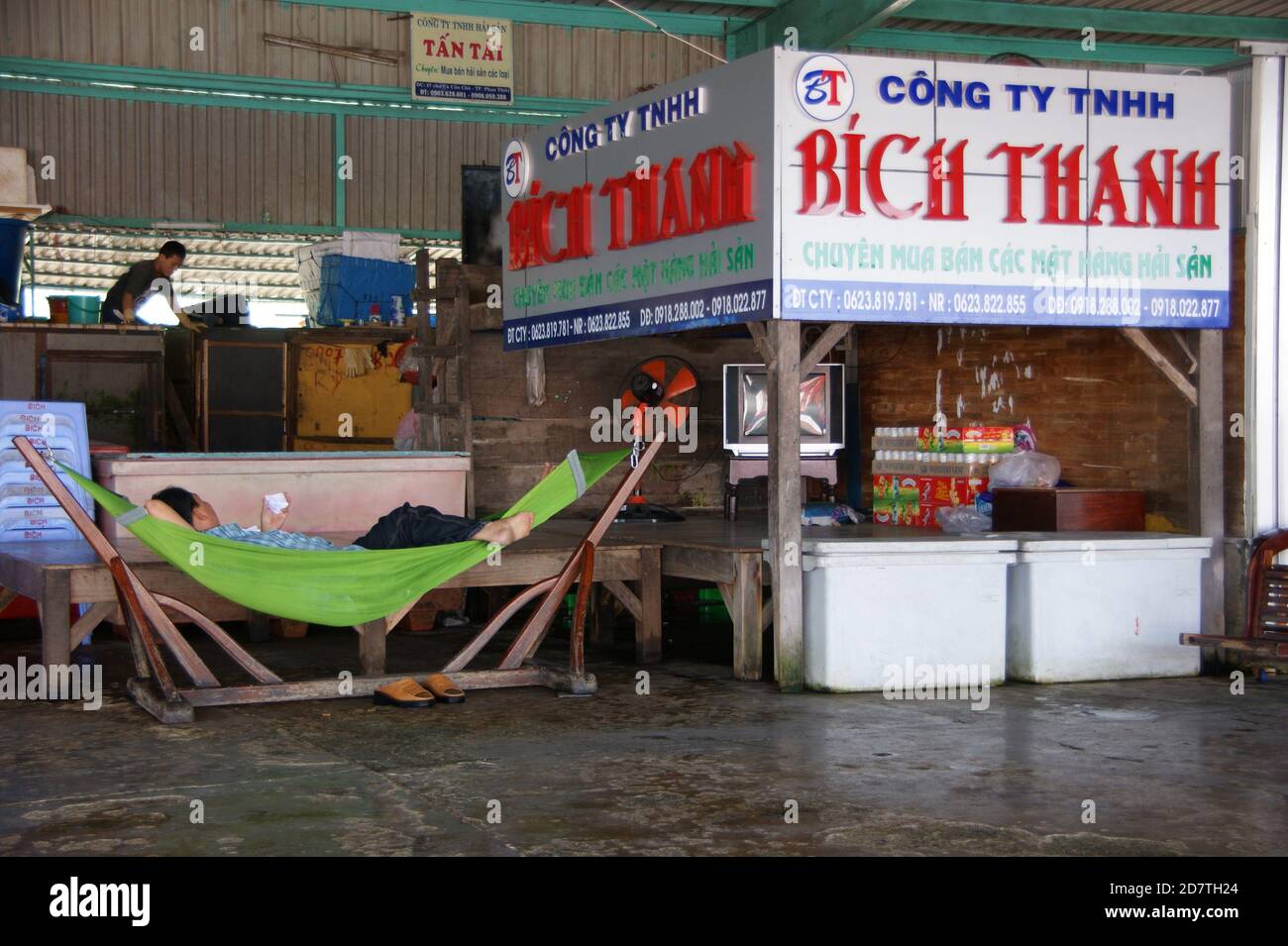 Erschöpfter Markthändler, der in einer Hängematte durch seinen fast leeren Stall ruht. Stockfoto