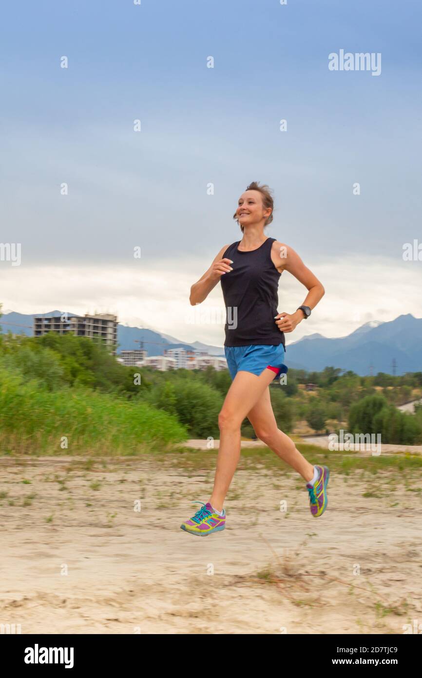 Laufen im Stadtpark. Frau Läuferin draußen beim Joggen, Blick auf die Berge im Hintergrund. Stockfoto