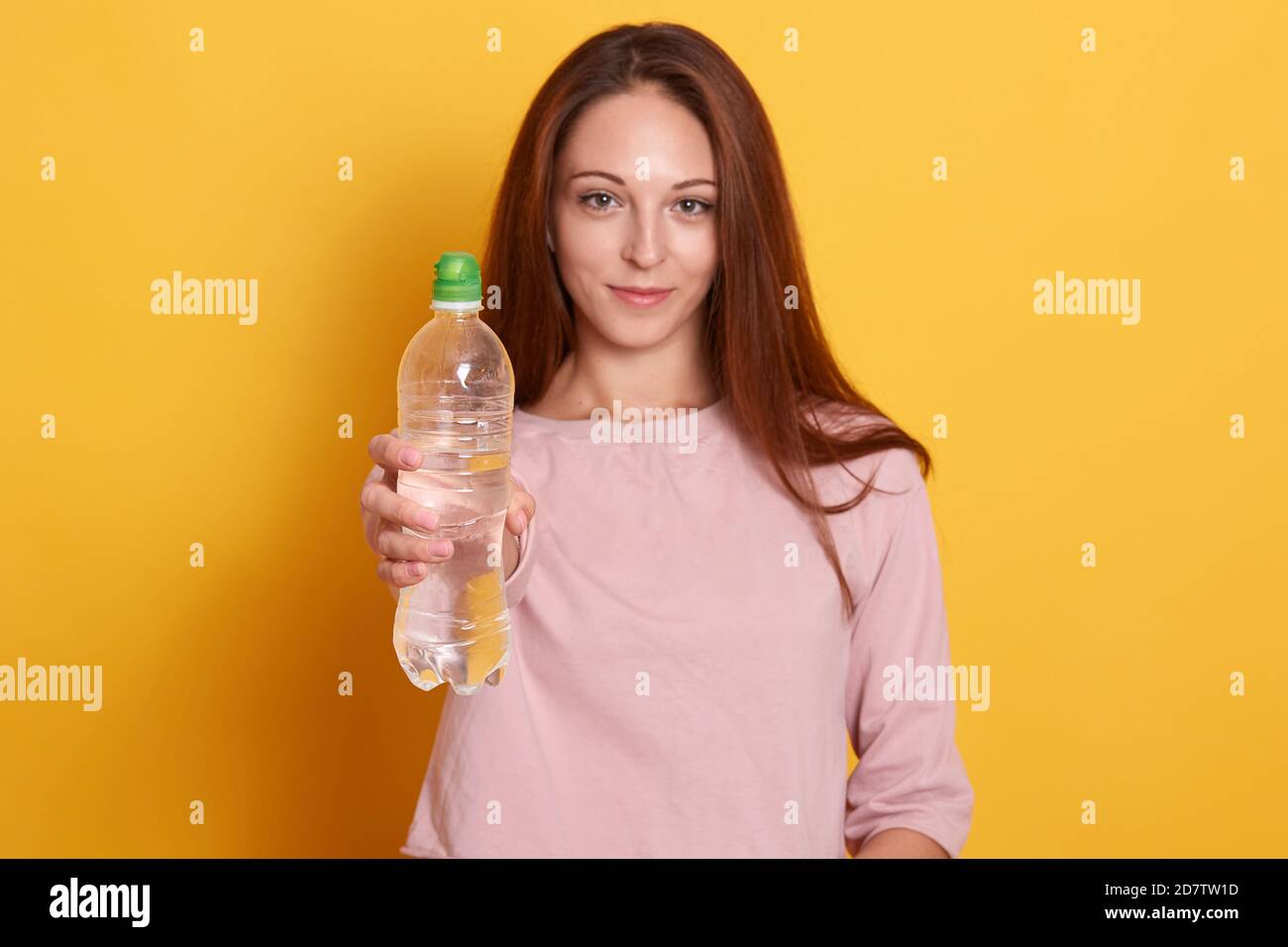 Portrait von schönen Sport Frau zeigt Flasche Wasser isoliert auf gelbem Hintergrund, Mädchen trägt rosa Hemd, attraktive famale mit langen braun Stockfoto