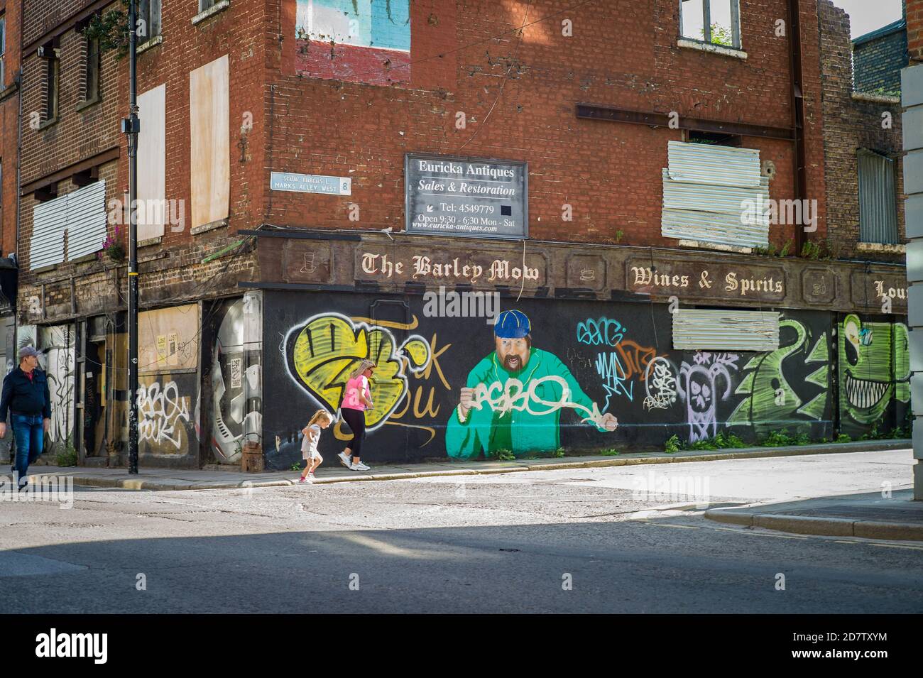 Die Menschen gehen an dem lang geschlossenen Barley Mow Pub in der Francis Street, Dublin, Irland vorbei. Das Wandbild ist von Brendan Grace. Grace war ein Iren gekommen Stockfoto