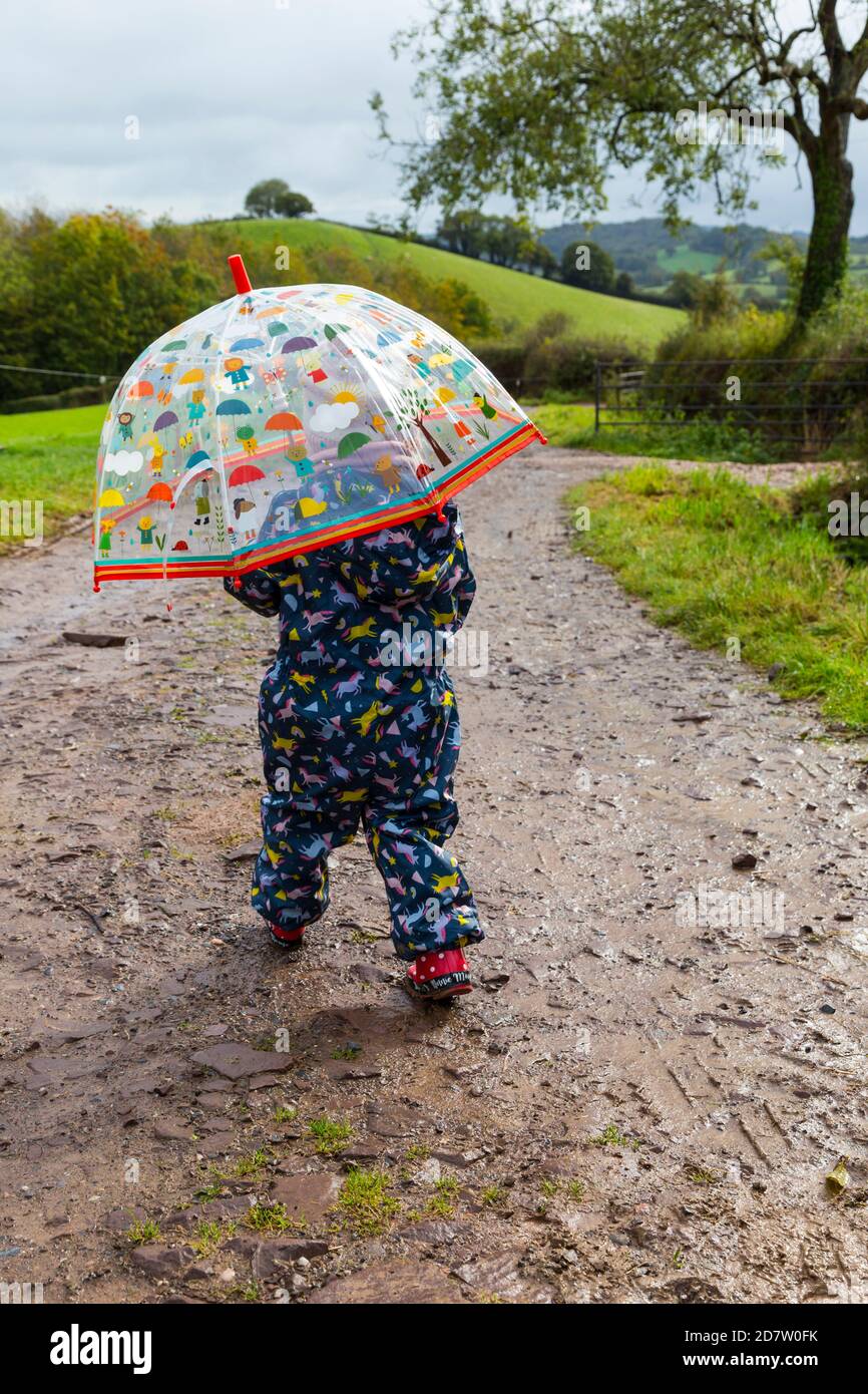 2 Jahre altes Kind, das im Regen entlang der Landstraße läuft und ihren  Regenschirm hält Stockfotografie - Alamy