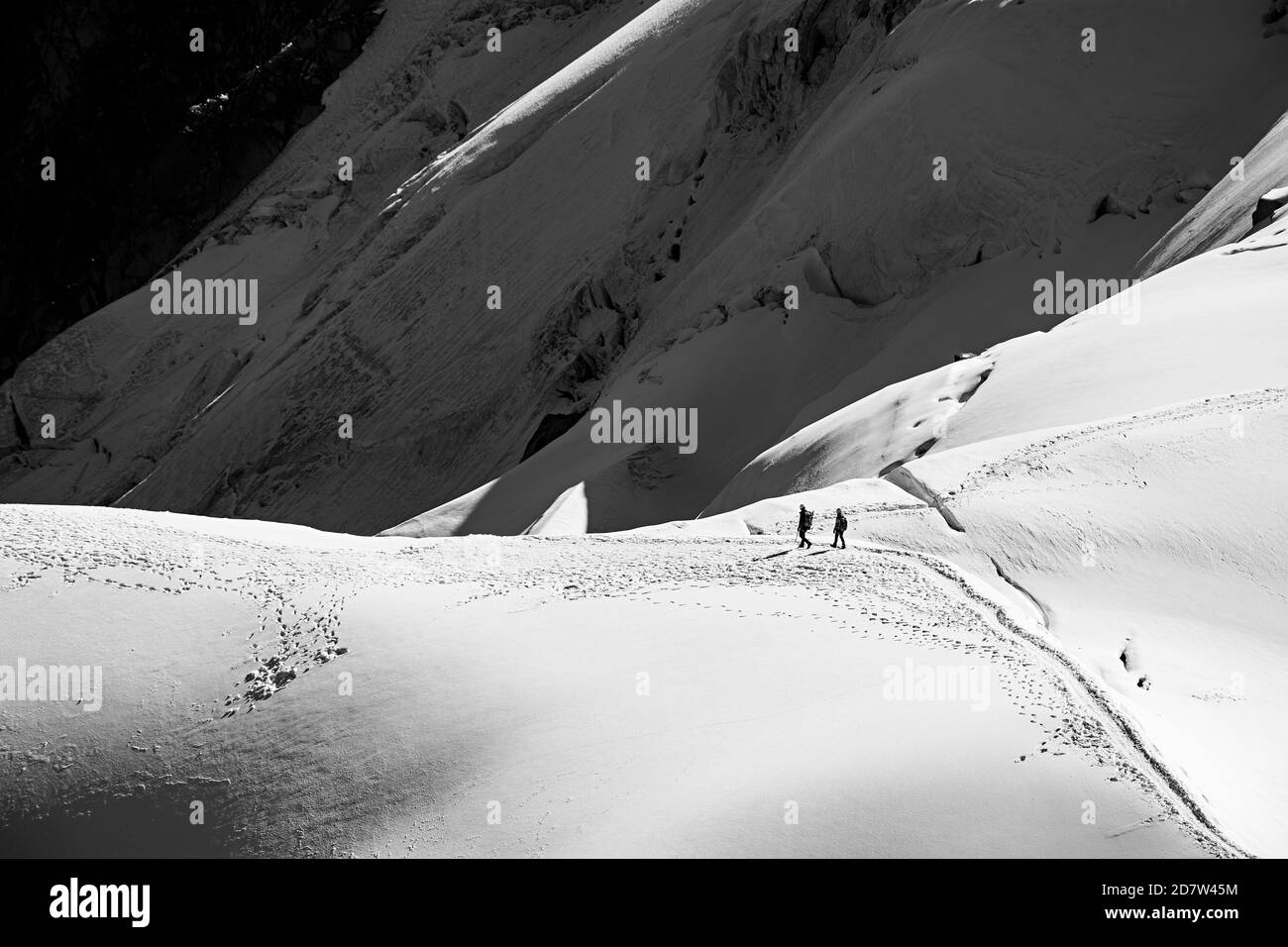 Trekker wandern auf einem verschneiten Bergrücken im White Valley, Mont Blanc Massiv von Aiguille du Midi 3842m, Chamonix, Frankreich. Schwarzweiß-Kreativbild. Stockfoto