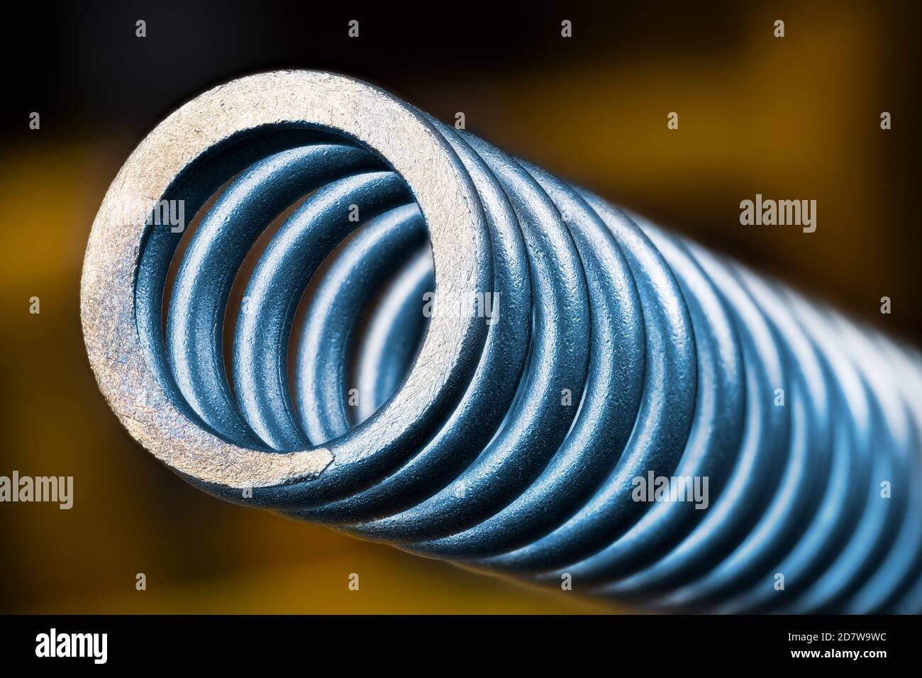 Schöne blaue Druckfeder aus legiertem Stahl. Künstlerische Details. Abstrakte Nahaufnahme eines elastischen mechanischen Geräts, um Energie zu speichern oder Stöße zu absorbieren. Stockfoto