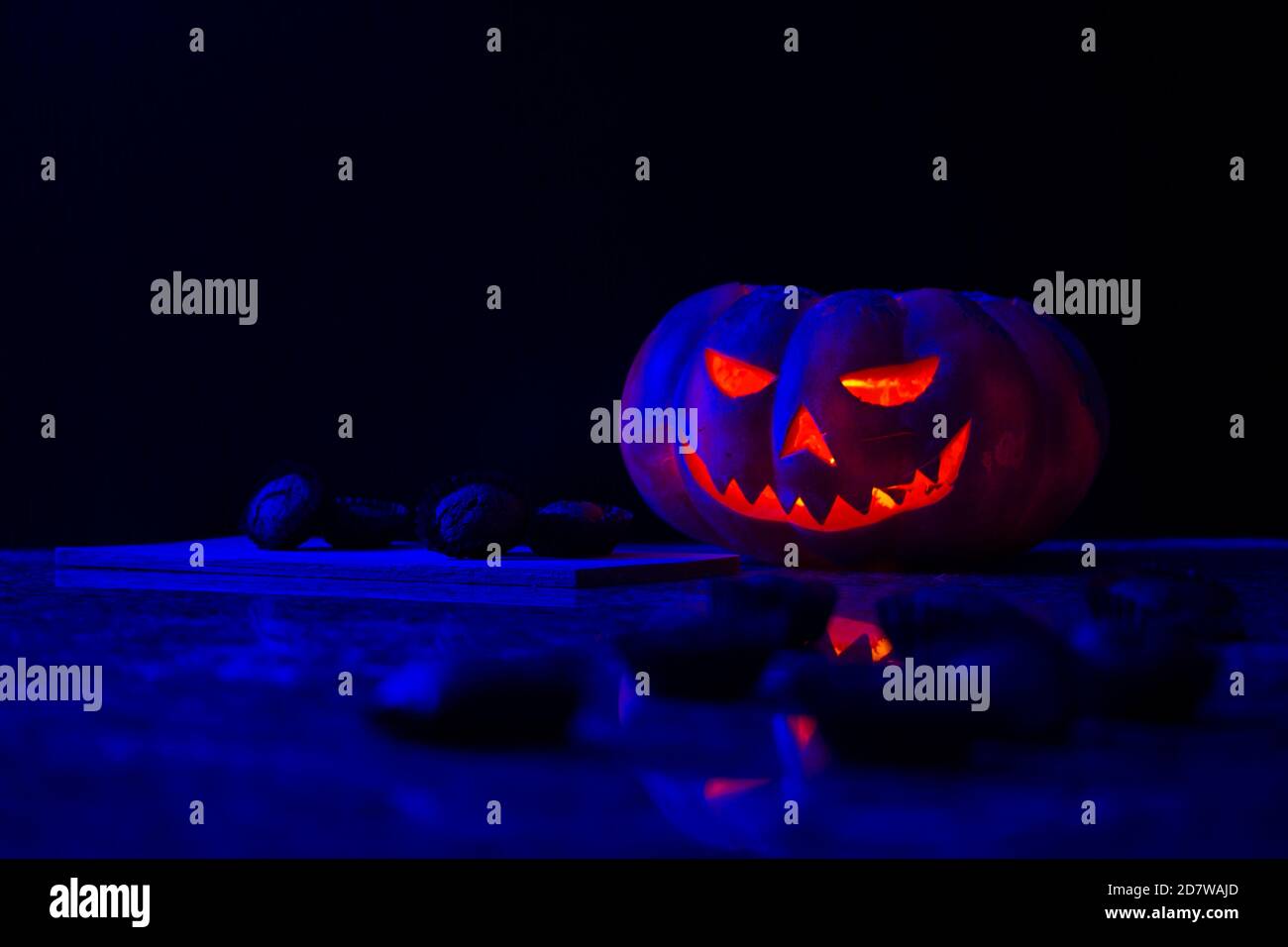 Halloween Kürbis mit einigen unscharf Kürbis Muffins im Vordergrund und mehr Muffins auf einem Holzbrett daneben, alles auf dunklem Hintergrund. Stockfoto