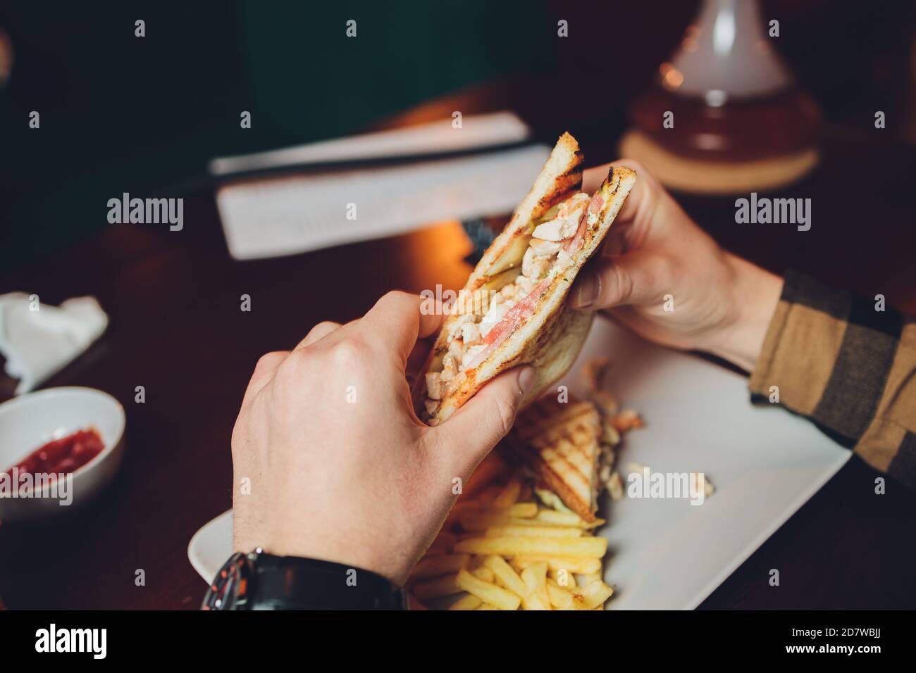 Der junge Mann bereitet sich glücklich, ein saftiges Veggie-Sandwich zu essen. Sandwich aus der Nähe, sichtbare Kichererbsen-Schnitzel, Tomaten und Salat. Stockfoto