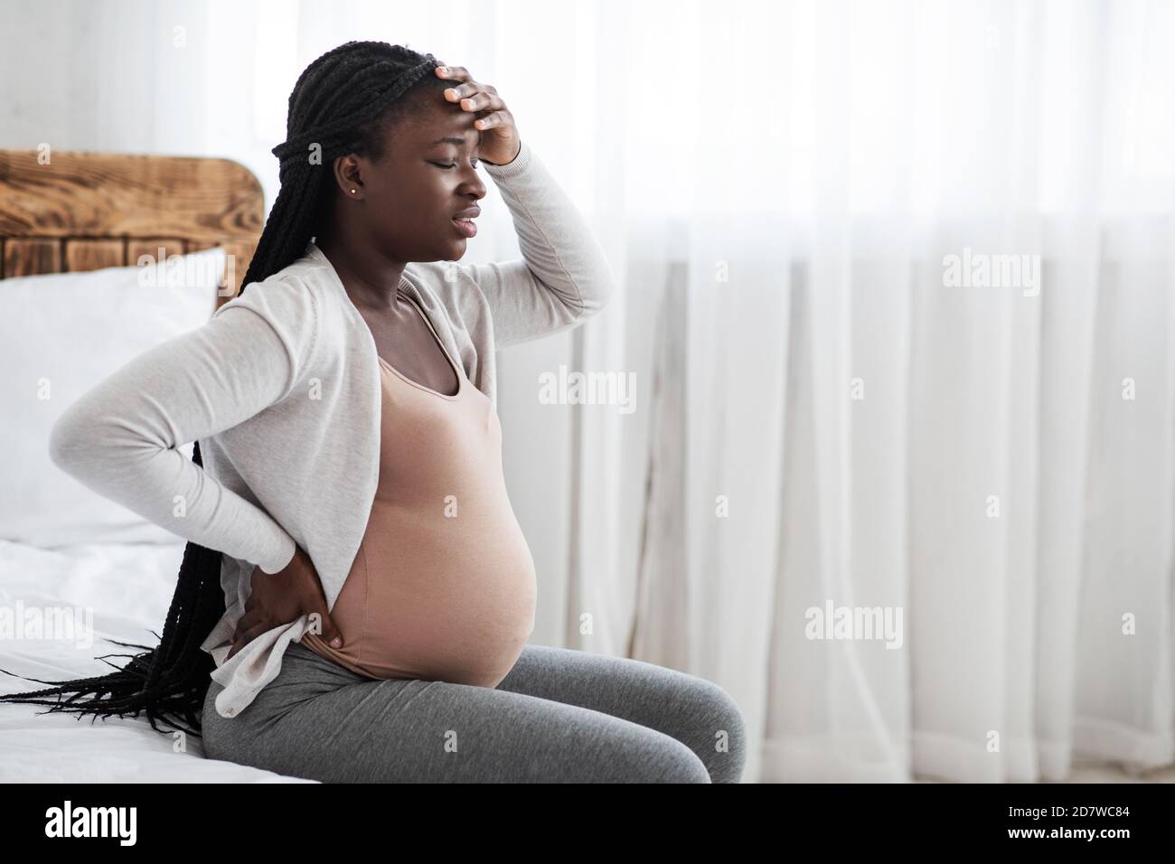 Krank African Schwangere Frau Gefühl Unwohl Zu Hause, Sitzend Auf Dem Bett Stockfoto