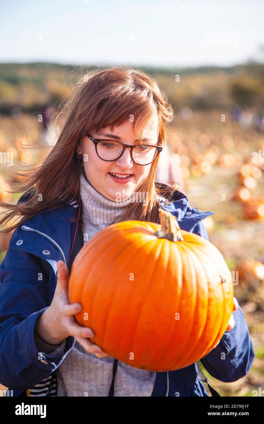 Eine junge Frau, die einen Kürbis hält und anschaut, ist gerade gepflückt, bereit für Halloween. Stockfoto