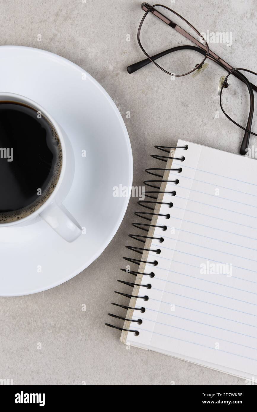 Flache Standzeit eines Business-Schreibtisches mit Kaffeetasse, Notizbuch und Brillen, vertikales Format. Stockfoto