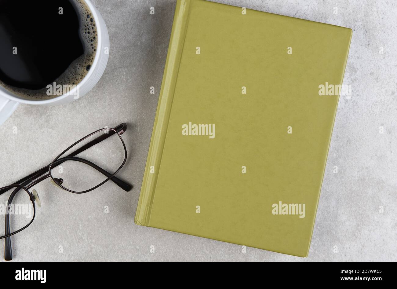 Flaches Stillleben eines Business-Schreibtisches mit Kaffeetasse, Bokk und Brillen auf einem hellgrauen Schreibtisch. Stockfoto