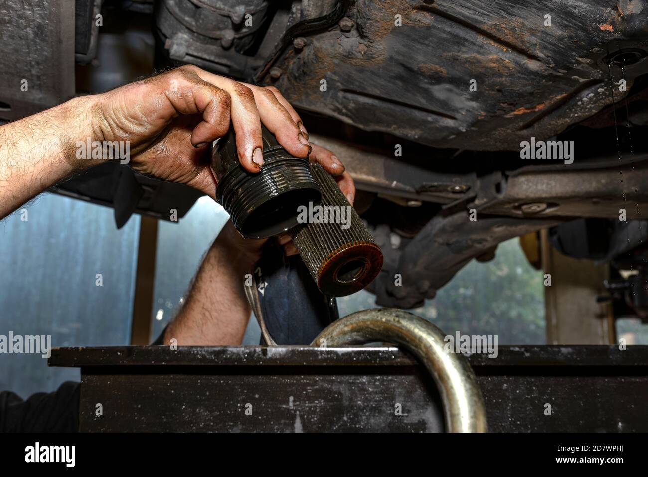 Automechaniker hält alten abgenutzten Ölfilter, Hände schmutzig mit schwarzem Öl. Stockfoto