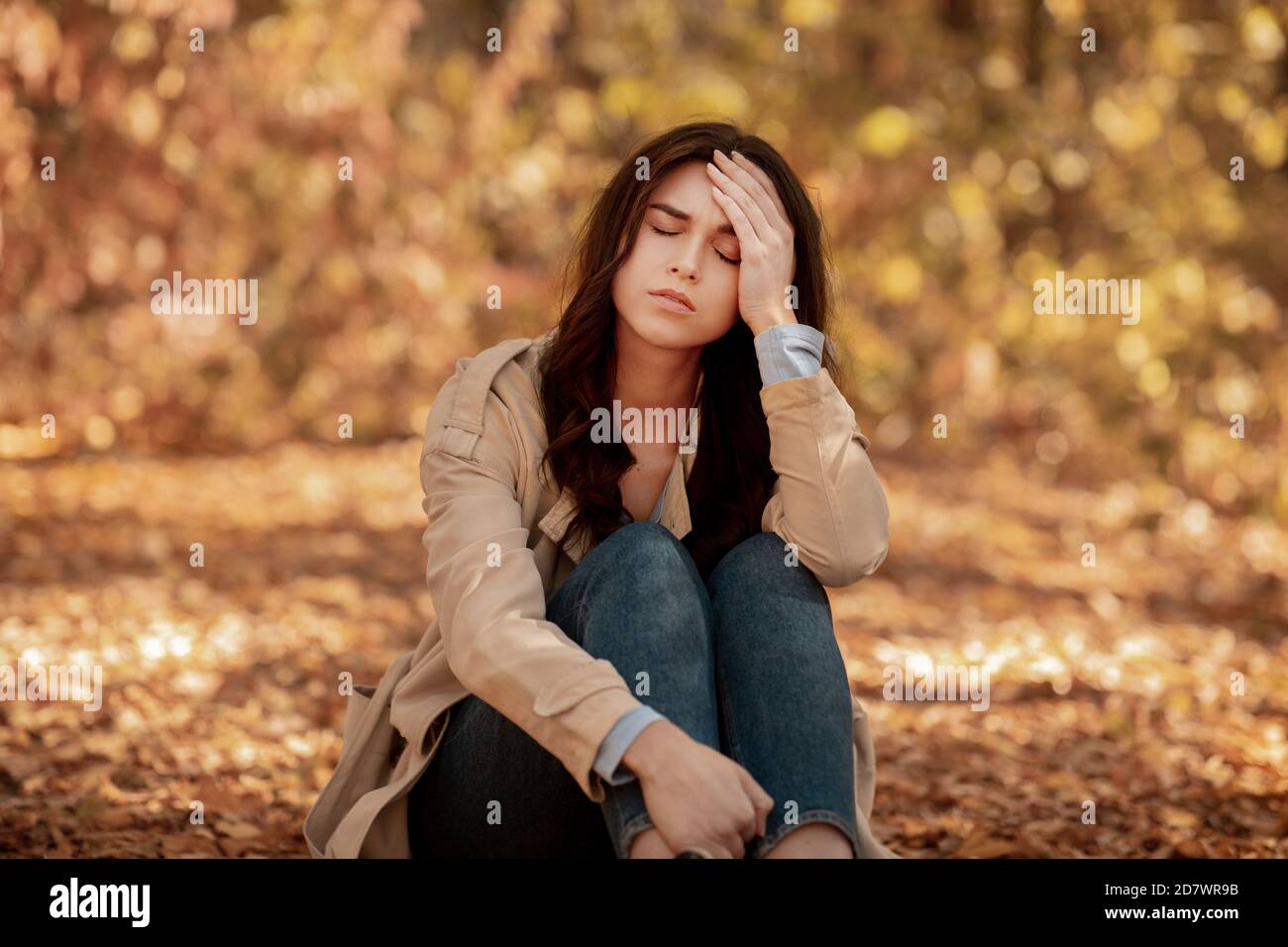 Müde oder depressive junge Frau, die im Herbst ihren Kopf berührt parken Stockfoto
